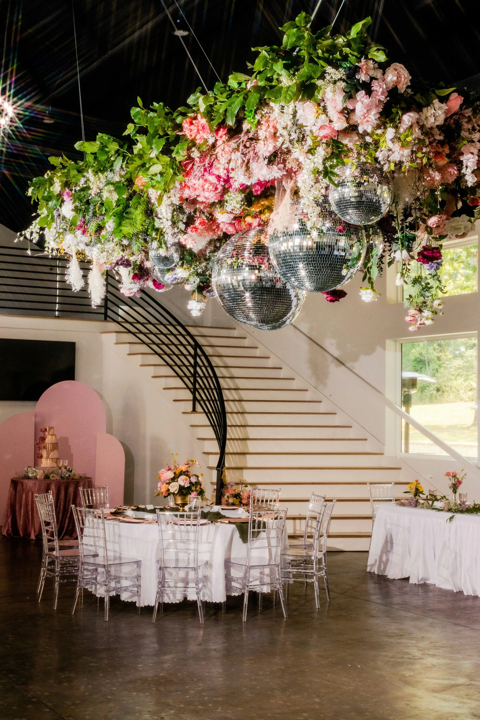 Elegant event space decorated with a large floral arrangement and disco balls hanging from the ceiling, with a table set for a celebration.