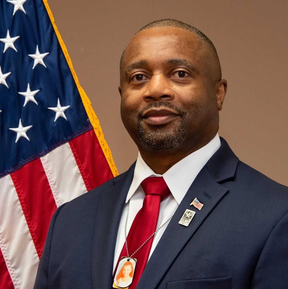 Rep. Kenneth Pascall in a dark suit with a red tie, standing in front of an American flag.
