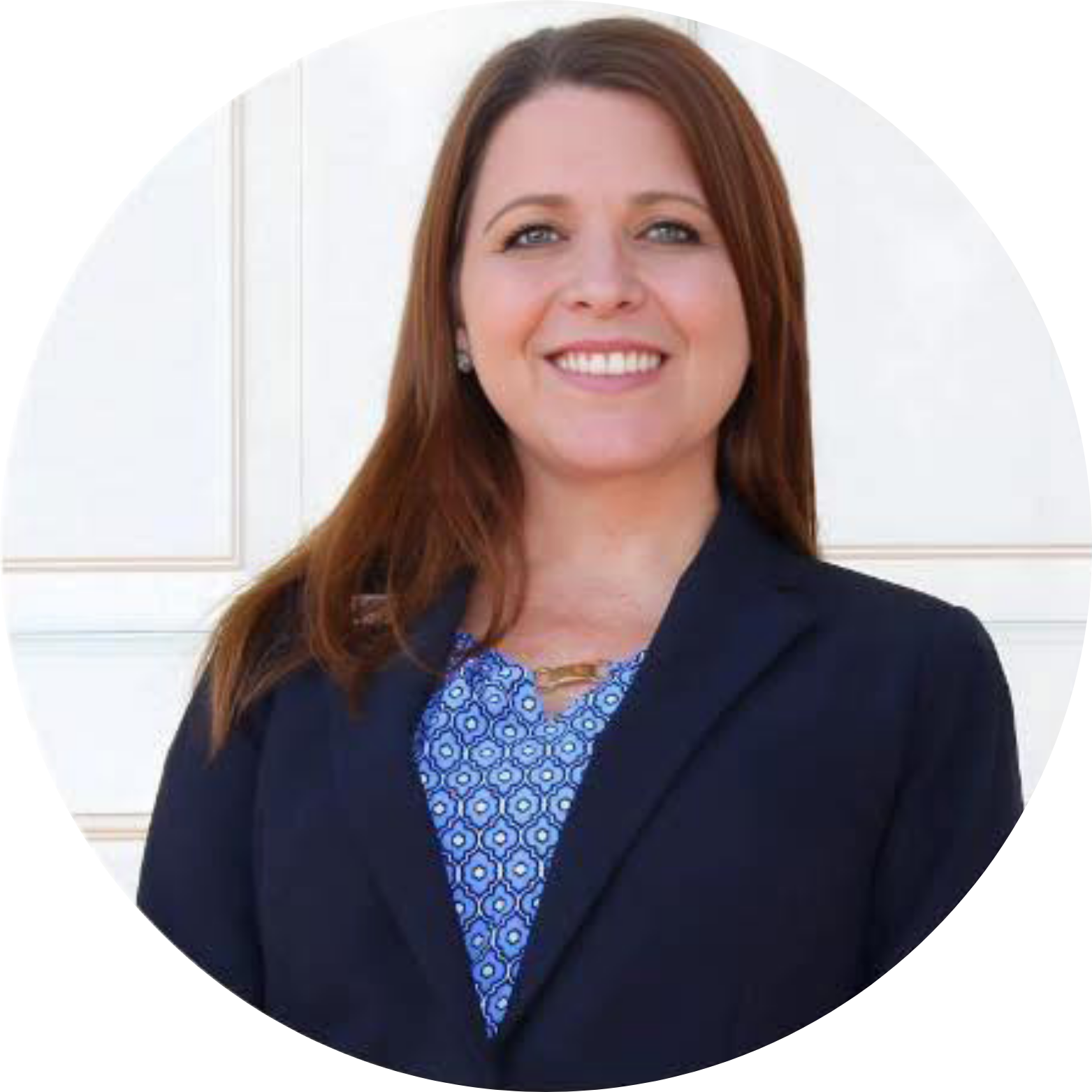 Natalie Steed with shoulder-length auburn hair, wearing a dark blazer and a blue patterned blouse, smiling in front of a plain white background.