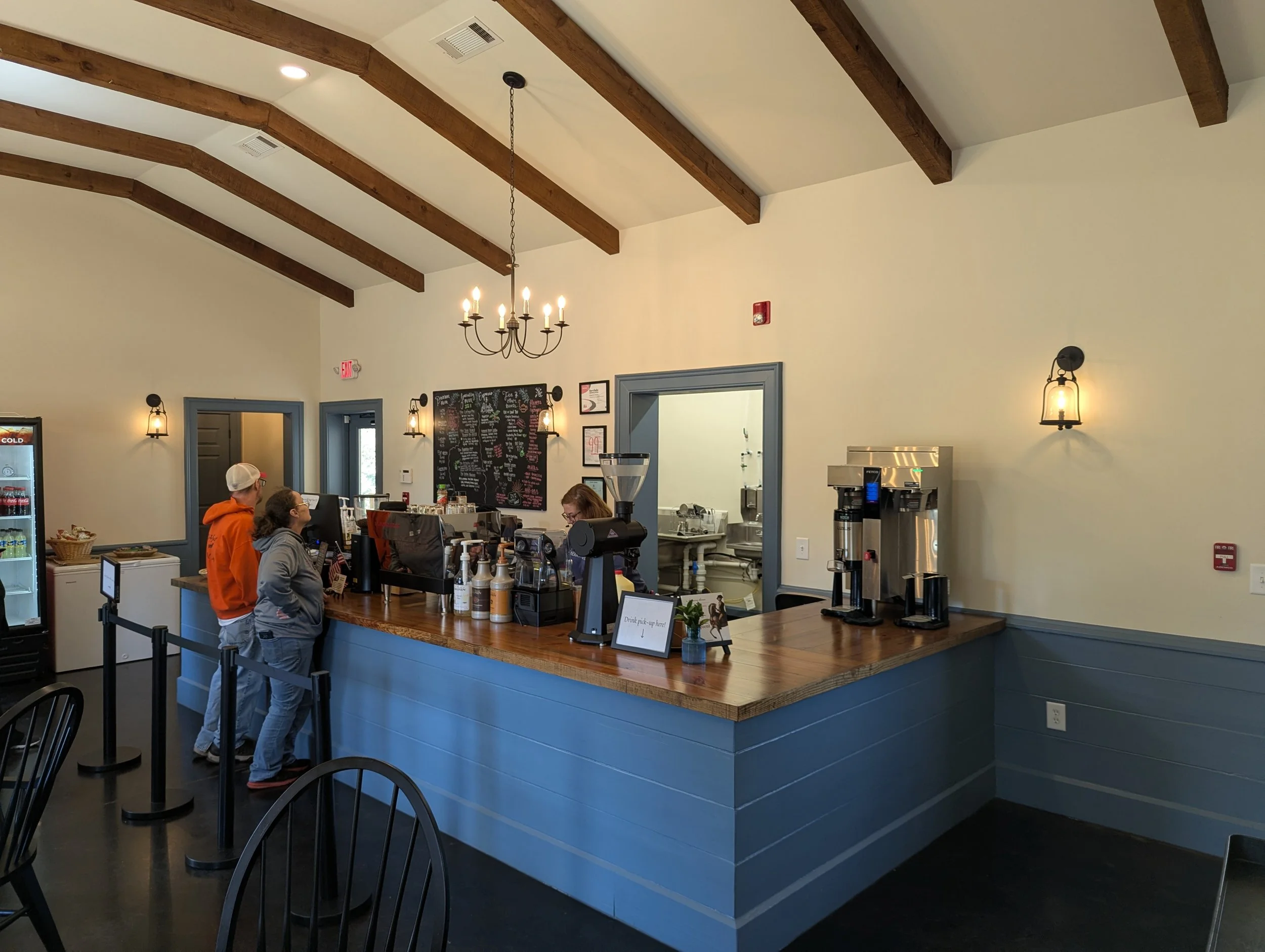 Customers at the counter of a cozy coffee shop with a wooden counter, chalkboard menu, and soft lighting