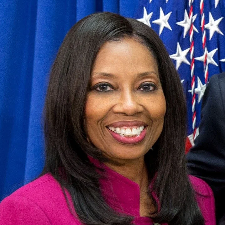 Dr. Geri Albright with straight, shoulder-length black hair smiling in front of an American flag.