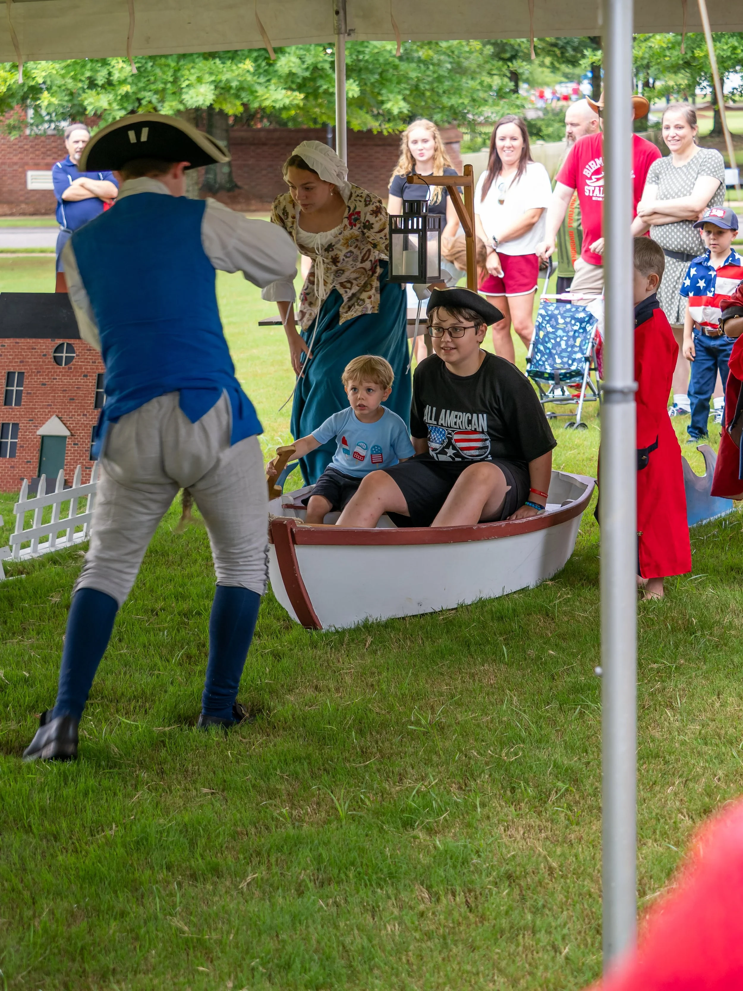 People dressed in colonial costumes demonstrating life in colonial times at an outdoor event.