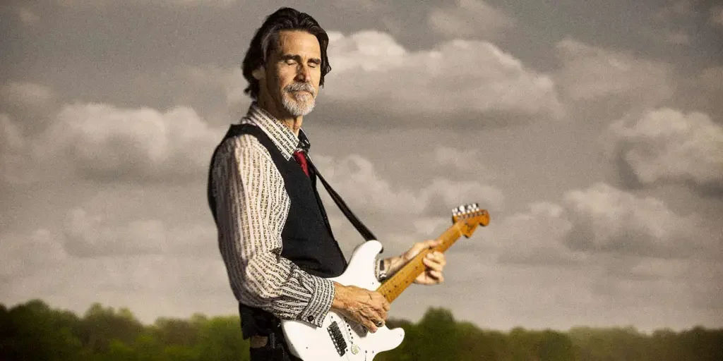 Will McFarlane playing an electric guitar outdoors under a cloudy sky.