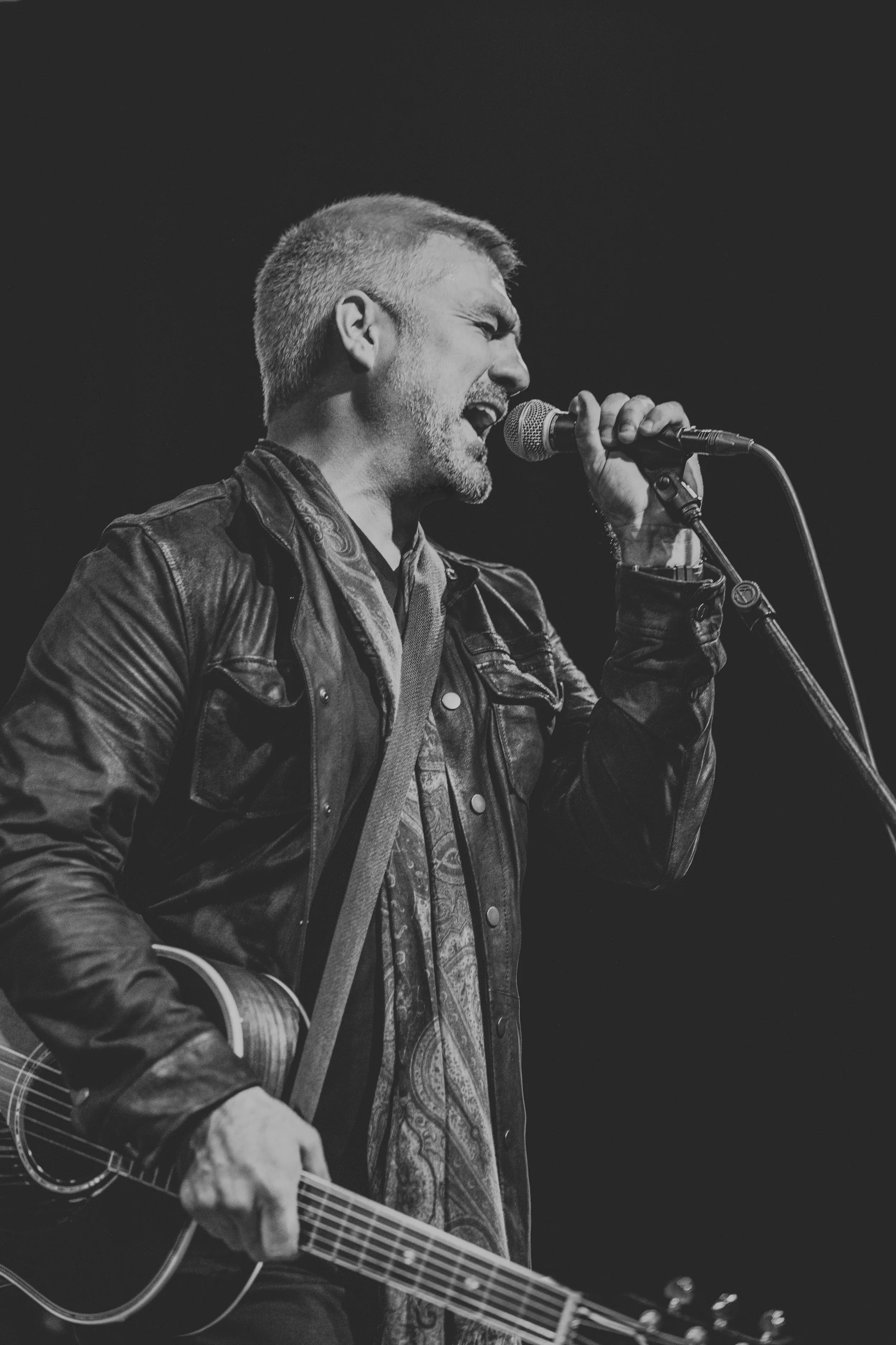 Taylor Hicks singing passionately into a microphone while playing an acoustic guitar.