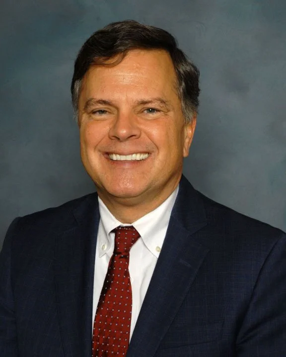 Sen. Arthur Orr in a dark suit, white shirt, and red patterned tie, against a plain gray background.