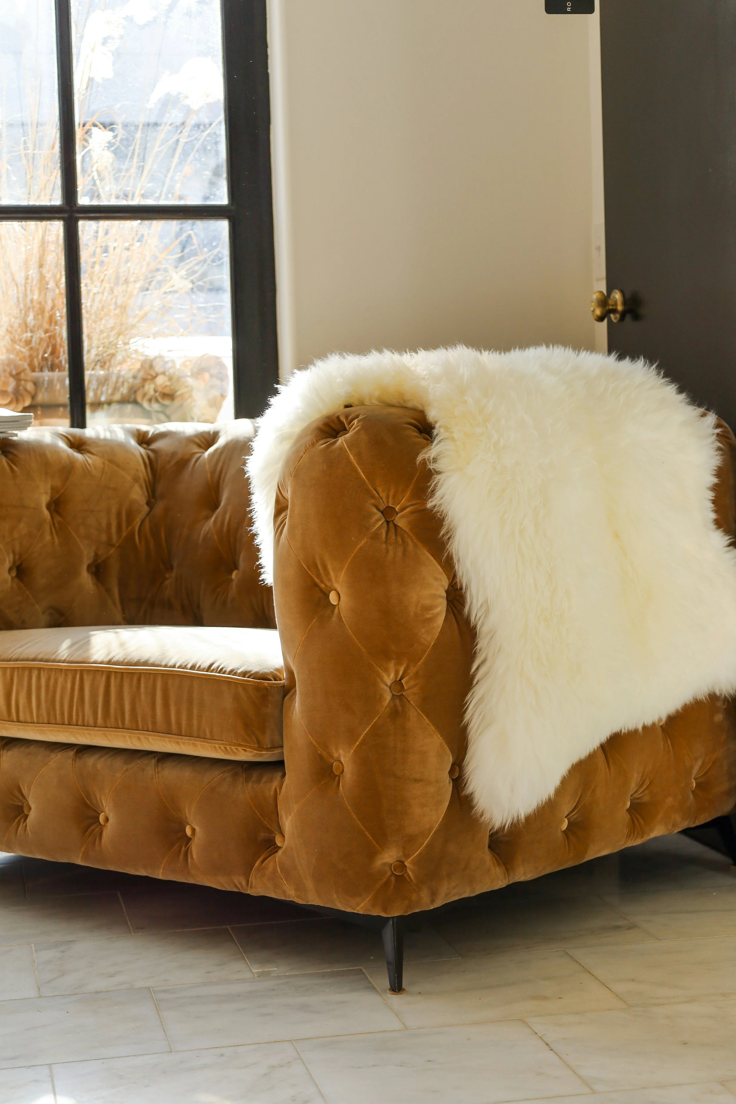 A brown tufted velvet sofa with a white faux fur throw blanket near a sunlit window, symbolizing the calm, welcoming space offered through therapy services in Raleigh, NC.
