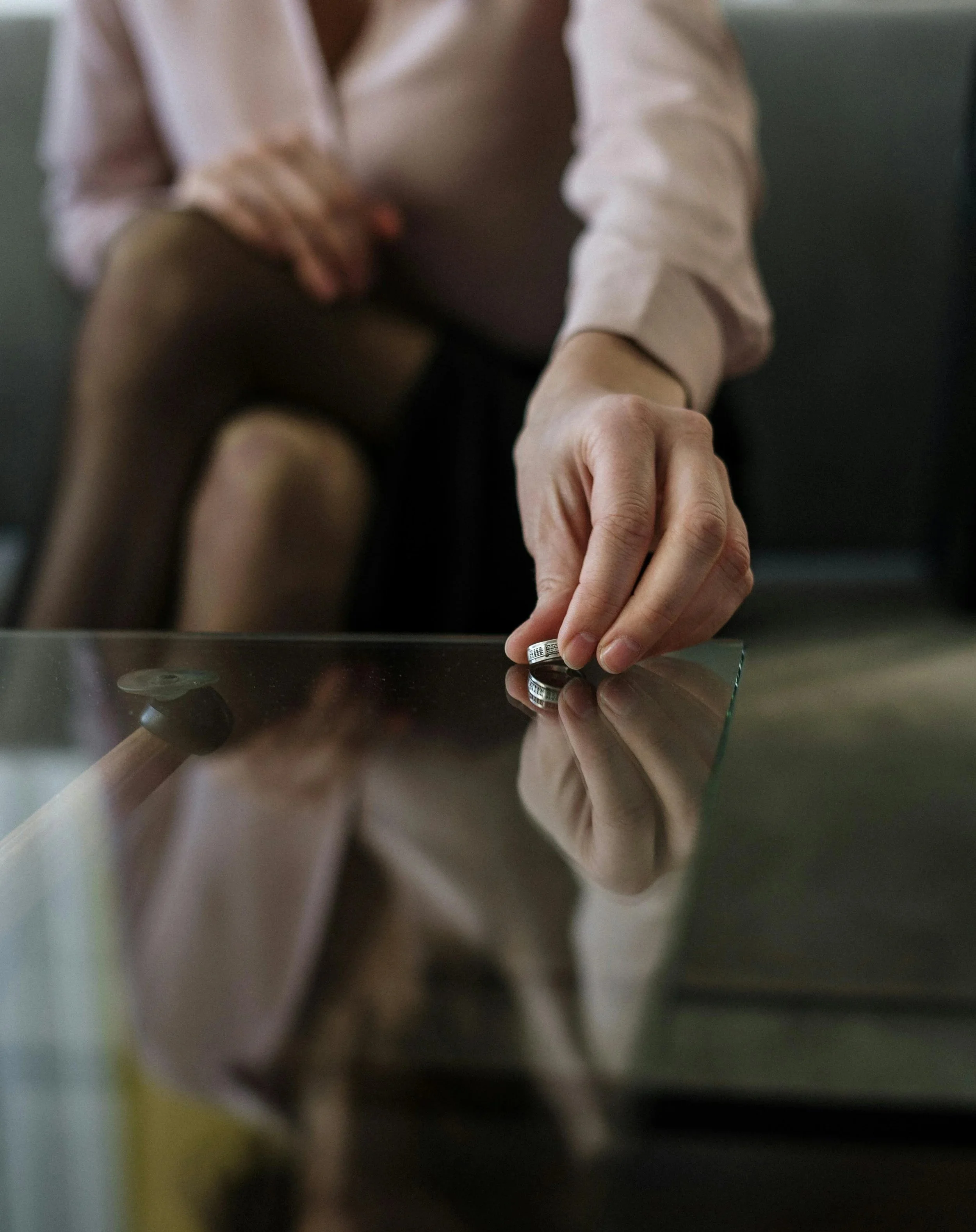 Person placing wedding rings on a glass table with reflection visible.