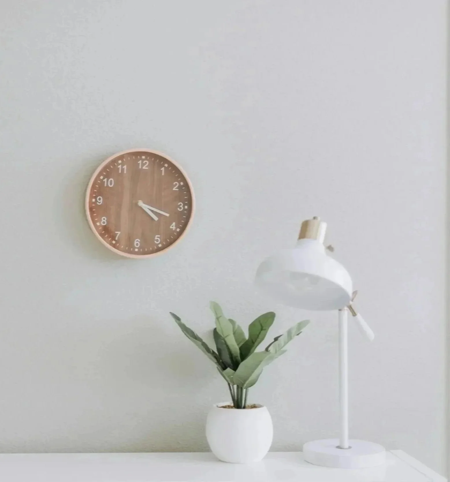 A clock reading 3:15 with a green plant and white desk lamp on a white surface, symbolizing the dedicated time and space offered in couples therapy intensives in Raleigh, NC.