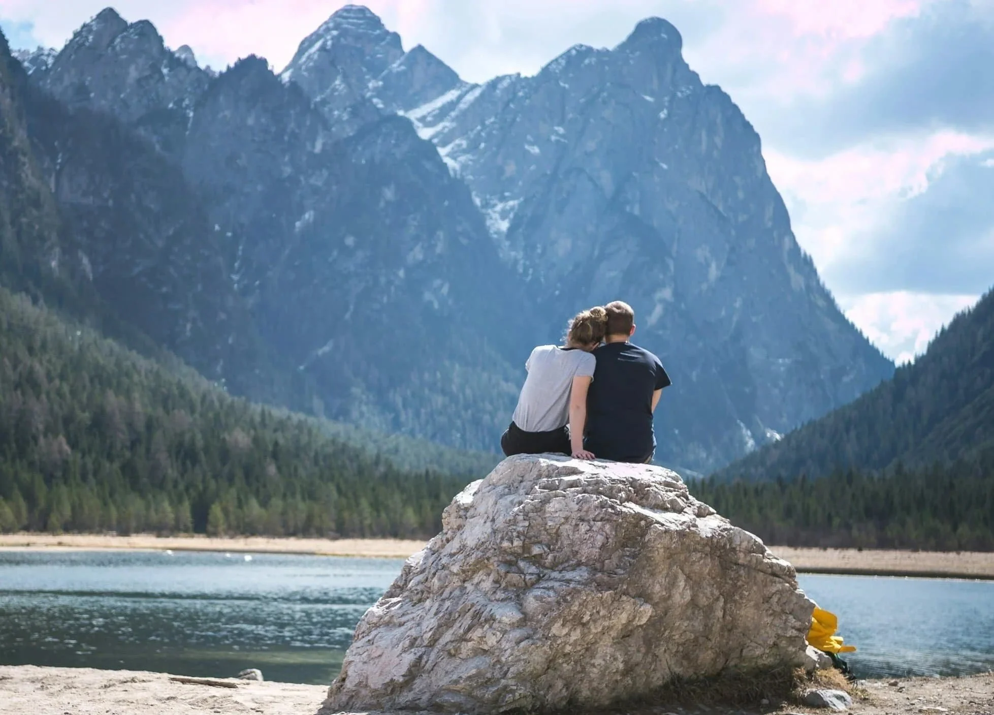 A couple sitting on a rock beside a lake and watching distant mountains and forests, symbolizing the healing and reconnection supported through infidelity counseling in Raleigh, NC.