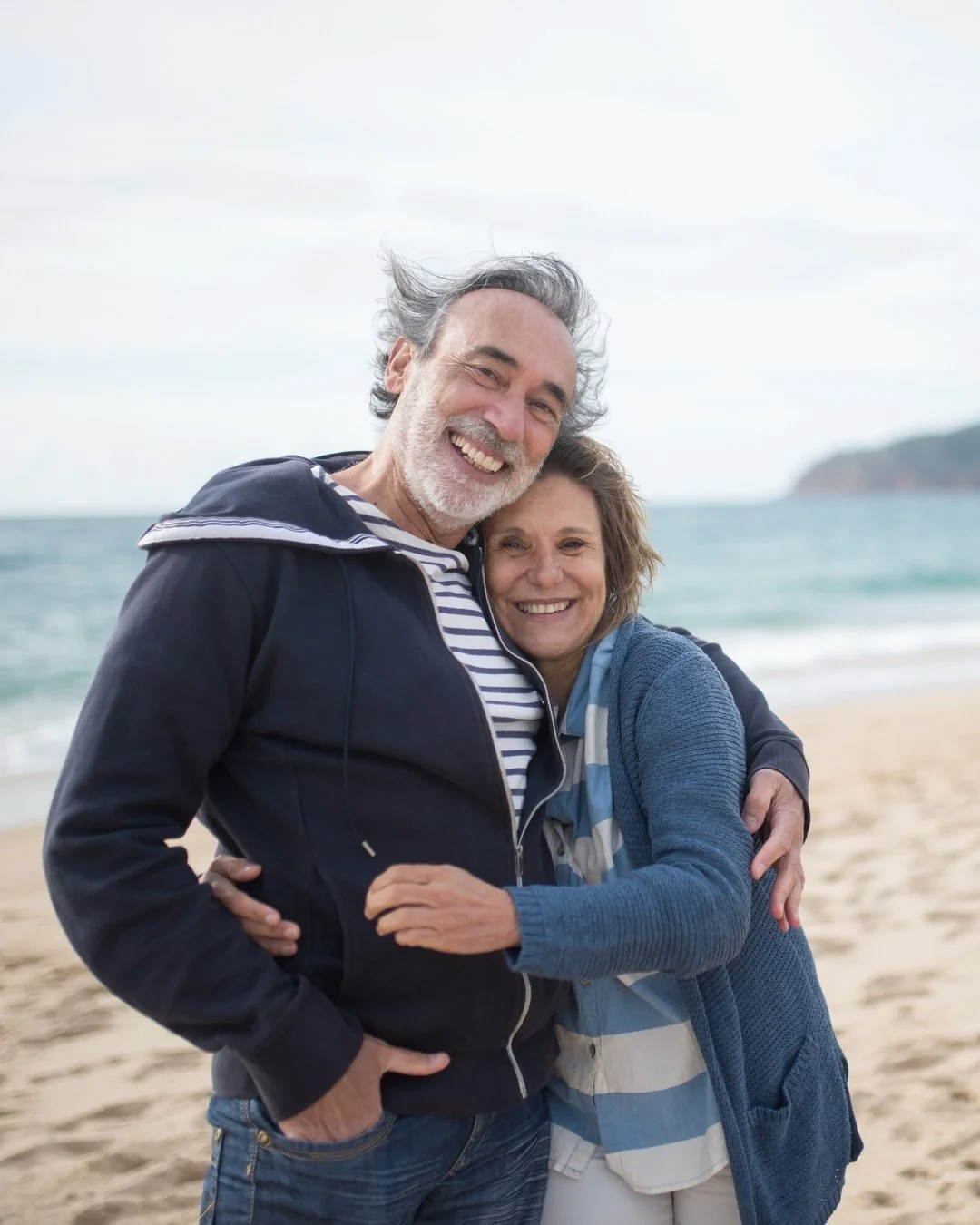 An elderly couple smiling and hugging at the beach, adding a warm, relational visual to Rising Tides Therapy Center in Raleigh, NC.
