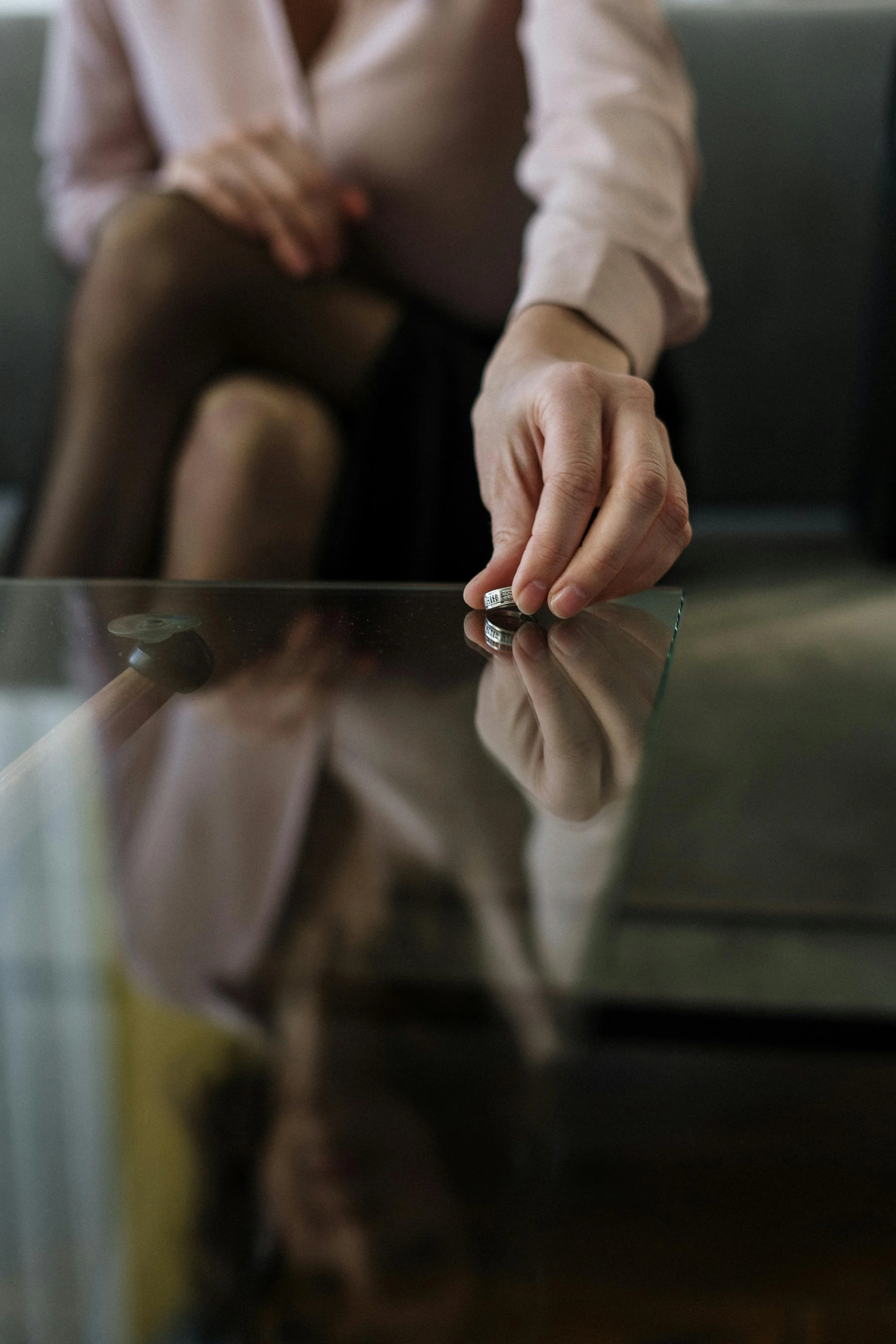 A woman placing wedding rings on a glass table in an office, with her reflection visible, symbolizing the healing and rebuilding supported through infidelity therapy in Raleigh, NC.