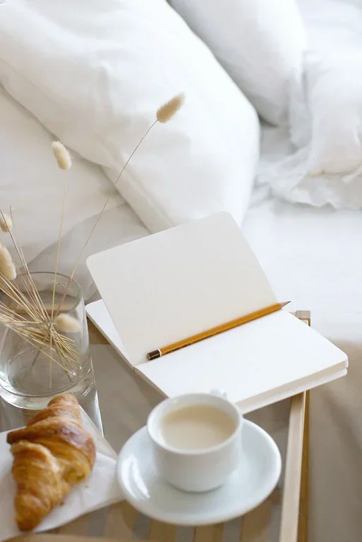 A side table in a Raleigh, NC therapy office featuring a glass of water, dried flowers, an open notebook, a pencil, coffee, and a croissant on white linens, symbolizing the supportive, reflective space offered through individual therapy.