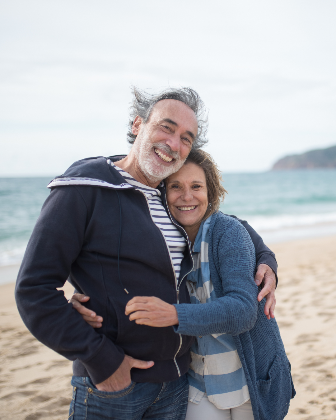 An elderly couple smiling and hugging at the beach, adding a warm, relational visual to Rising Tides Therapy Center in Raleigh, NC.