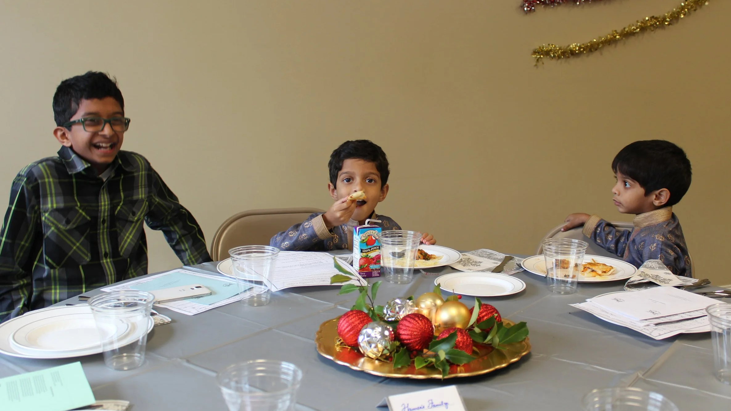 Three young boys sitting at a holiday dinner table with holiday decorations, eating pizza and juice.