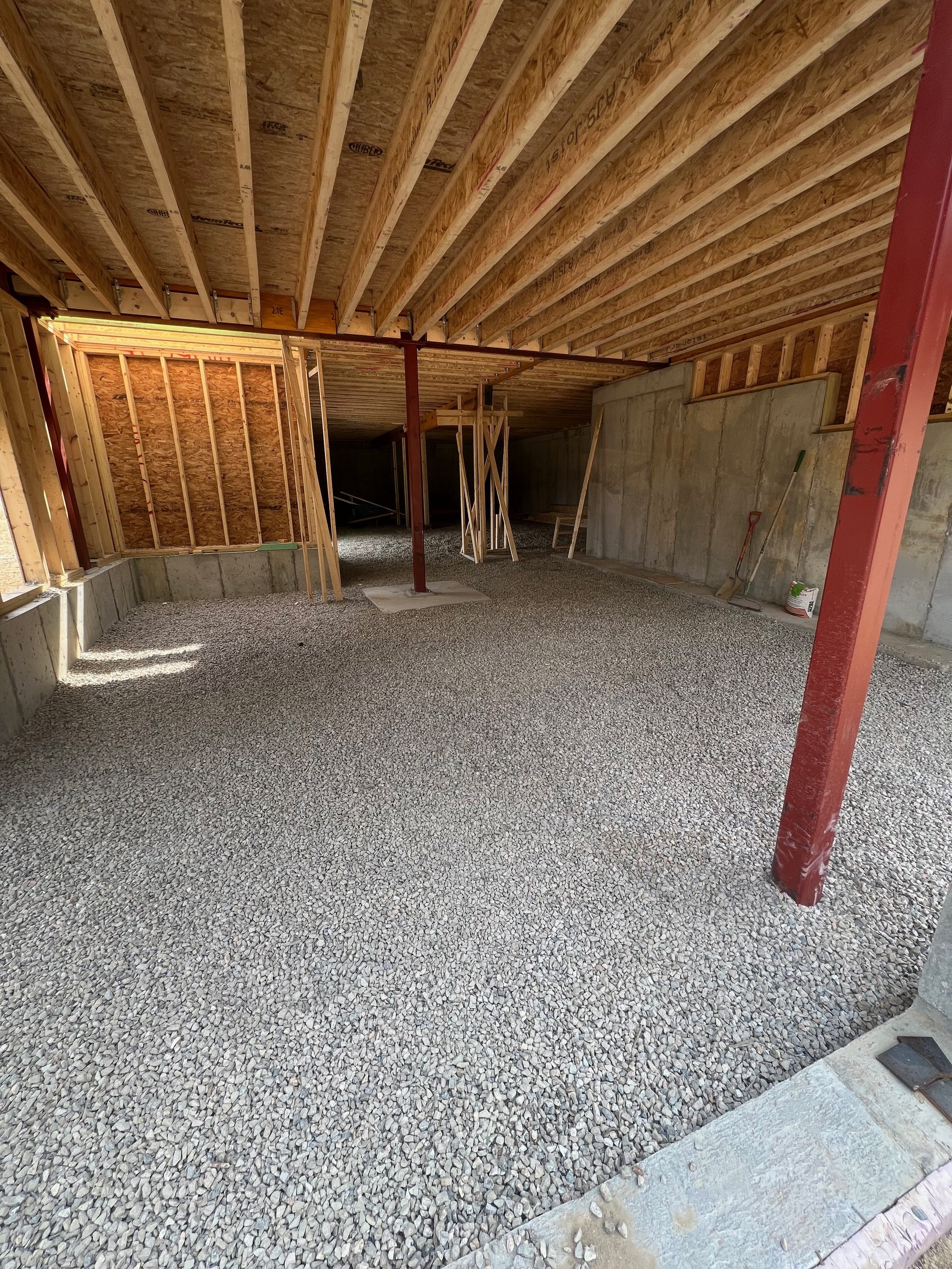 The interior of a building under construction, with exposed wooden framing, gravel floor, and support beams.