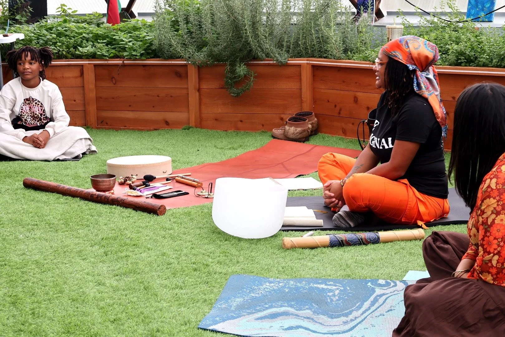 A young girl sitting cross-legged on a blanket, listening to a woman speaking during a sound healing event for soul sprouts