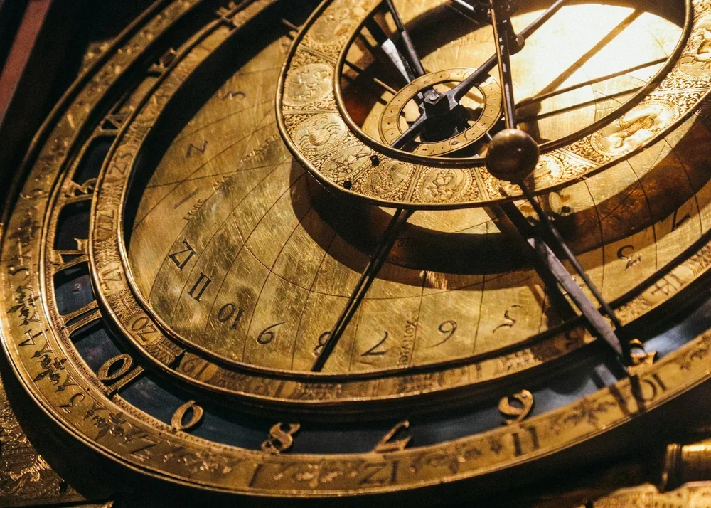Close-up of an ornate, antique astronomical clock with gold details and Roman numerals.