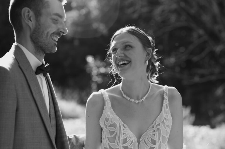 A bride and groom smiling at each other outdoors during their wedding.