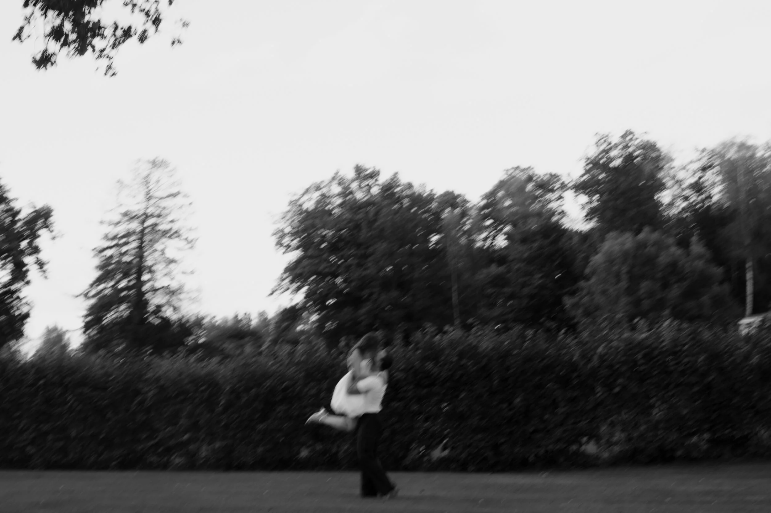 A person lifting a child in the air outdoors with trees in the background, black and white image