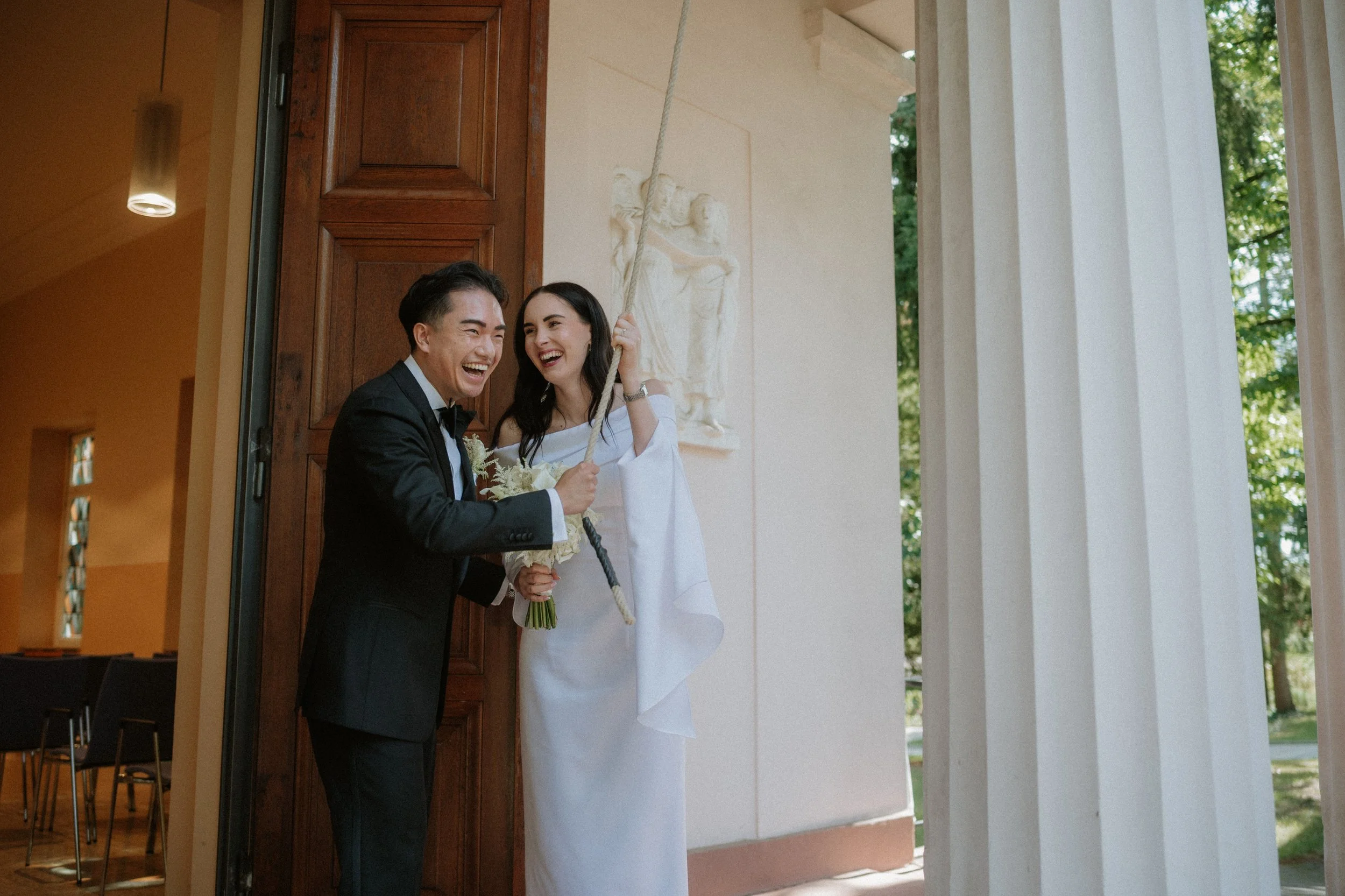 Happy bride and groom sharing a joyful moment outdoors, bride holding a bouquet and swinging on a rope.