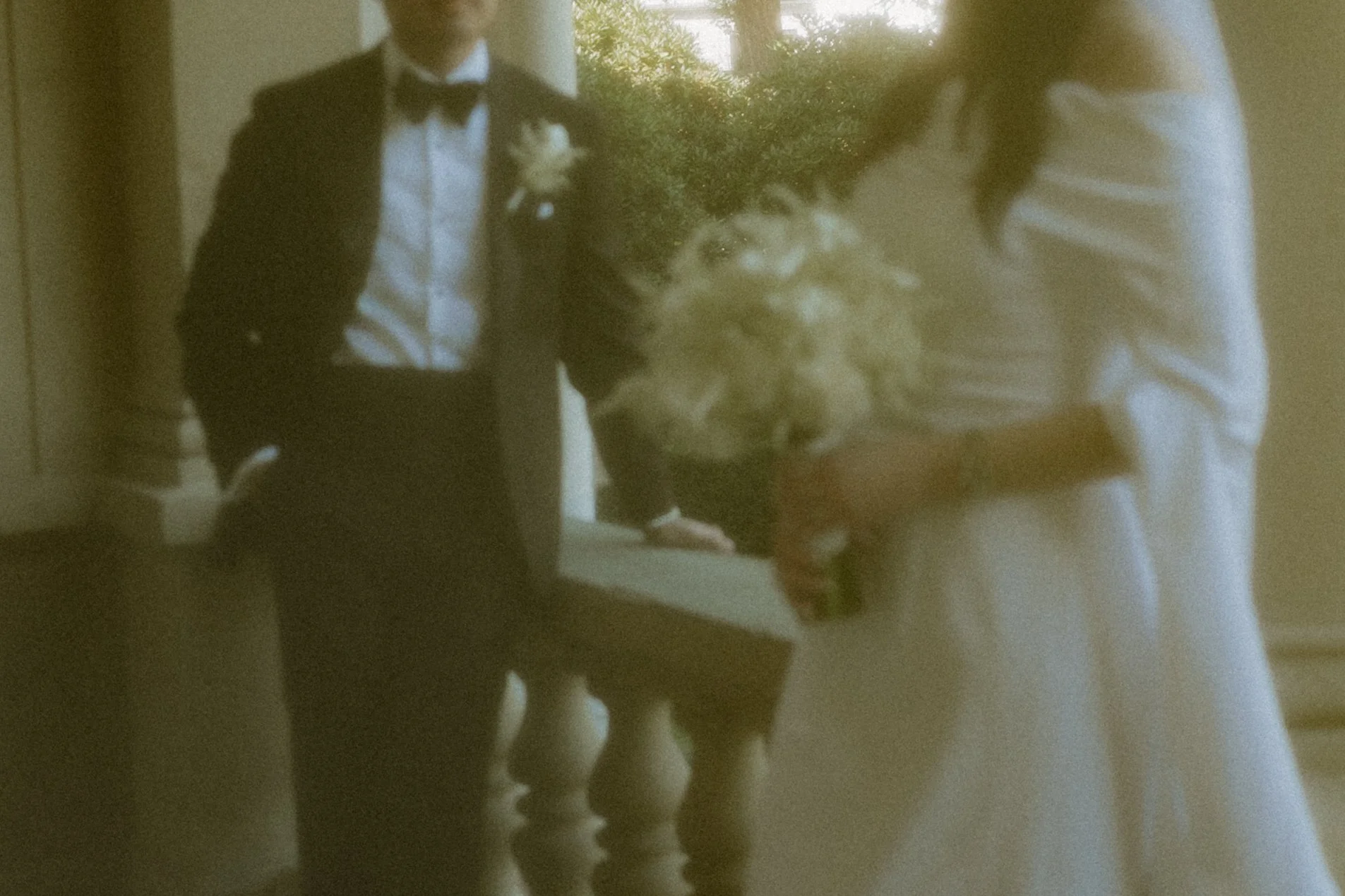 A man in a tuxedo holding a bouquet of flowers, standing on a staircase, with a woman in a striped shirt holding a lion plush toy in front of her.