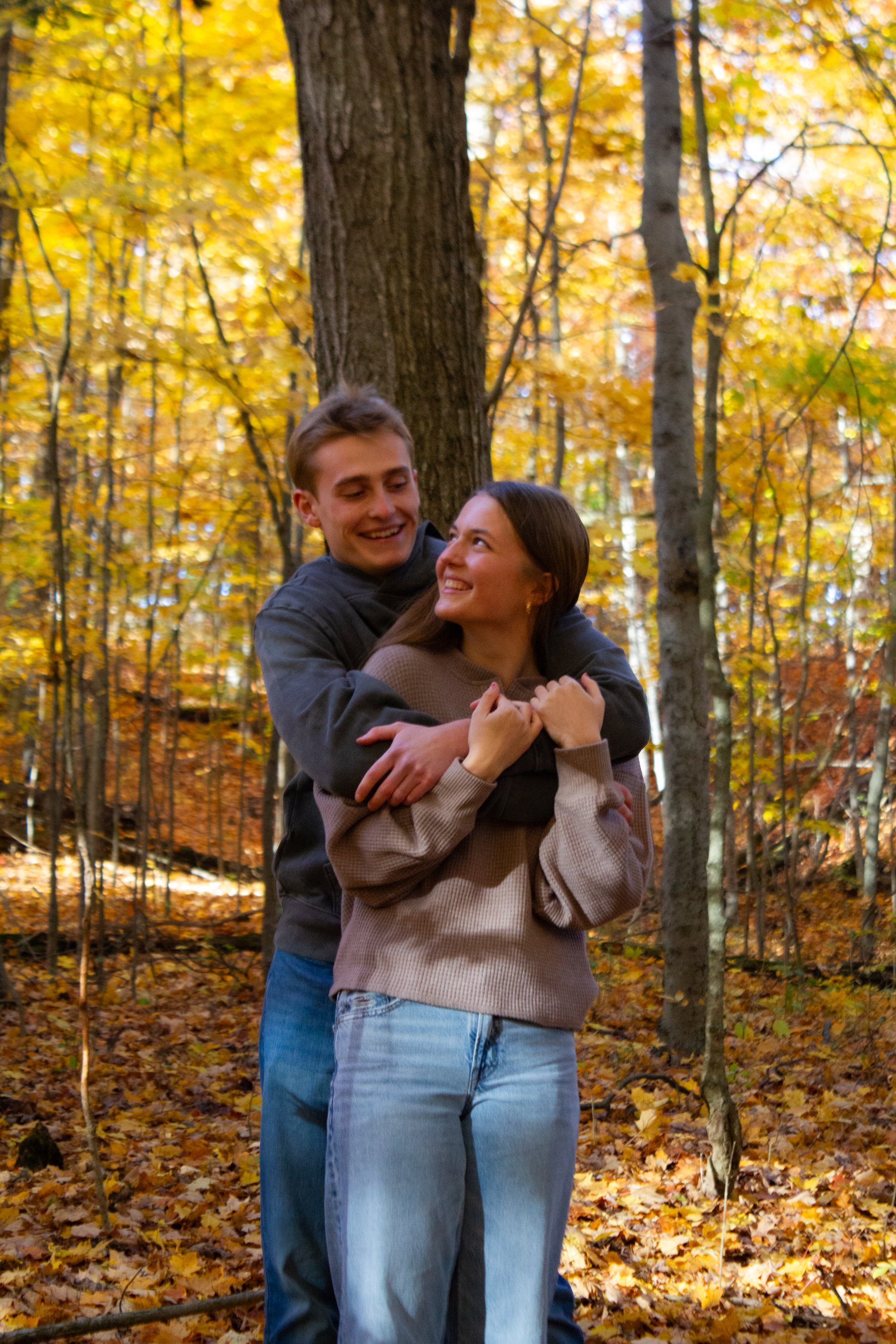 A young couple hugging and smiling in an autumn forest with yellow and orange leaves.