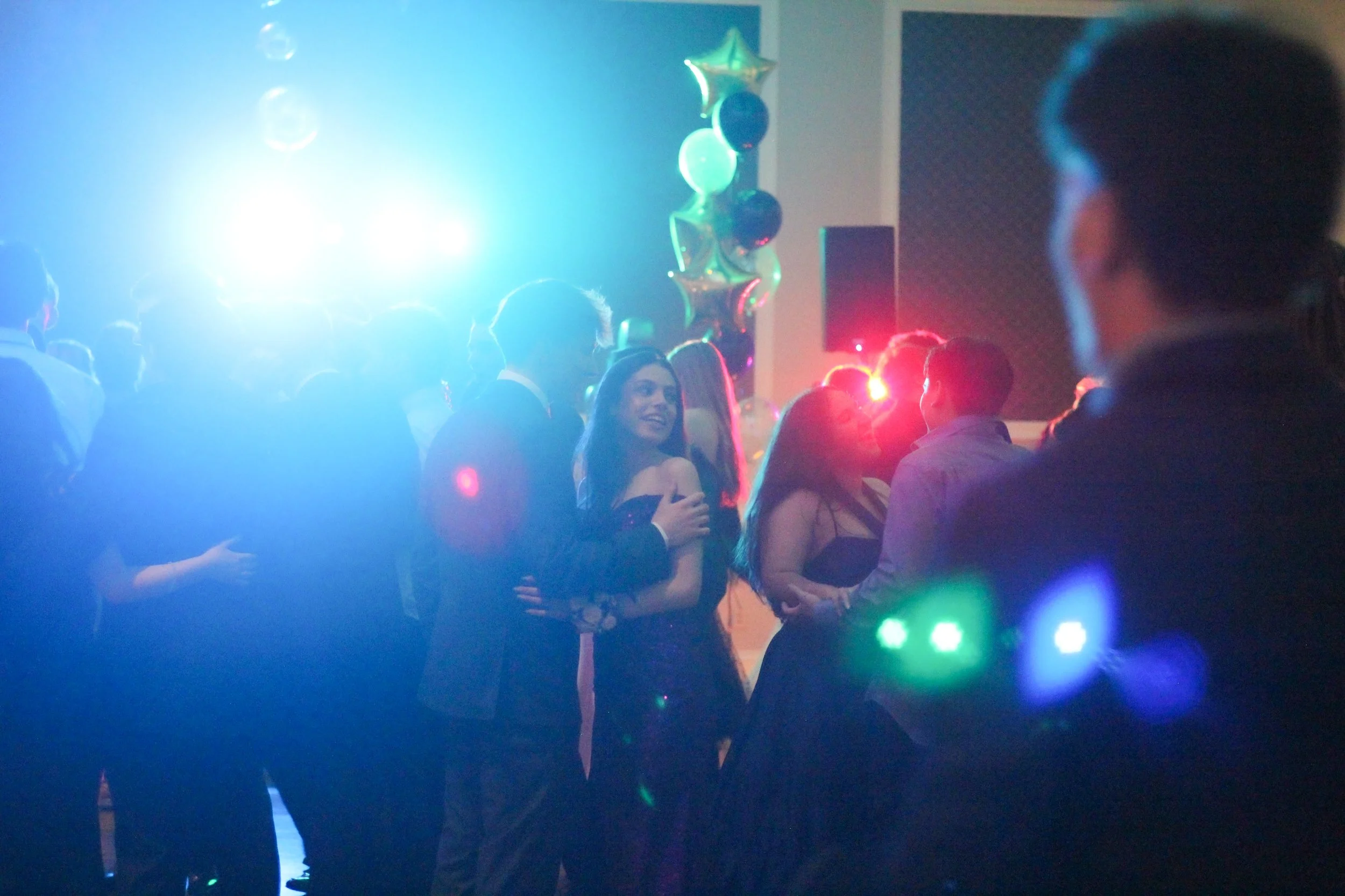 People dancing at a party with colorful lights and balloon decorations.