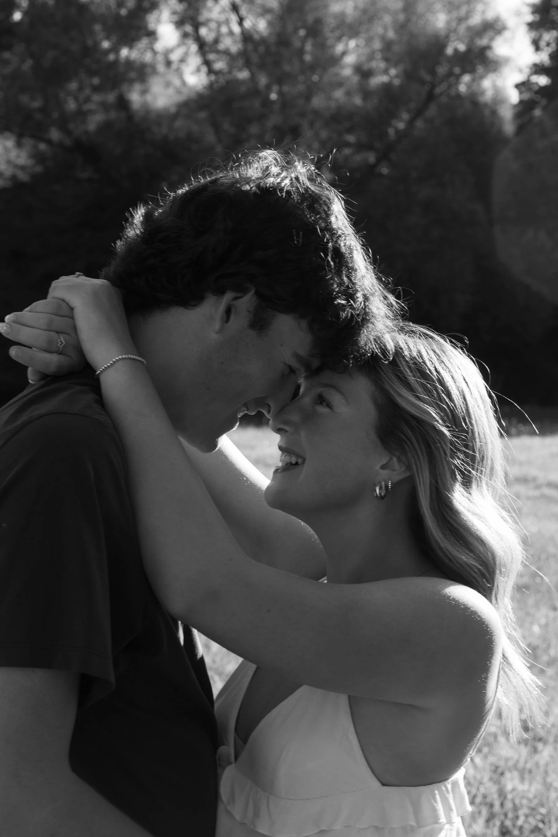 A couple in an outdoor setting sharing a joyful moment, touching their foreheads together and smiling at each other.