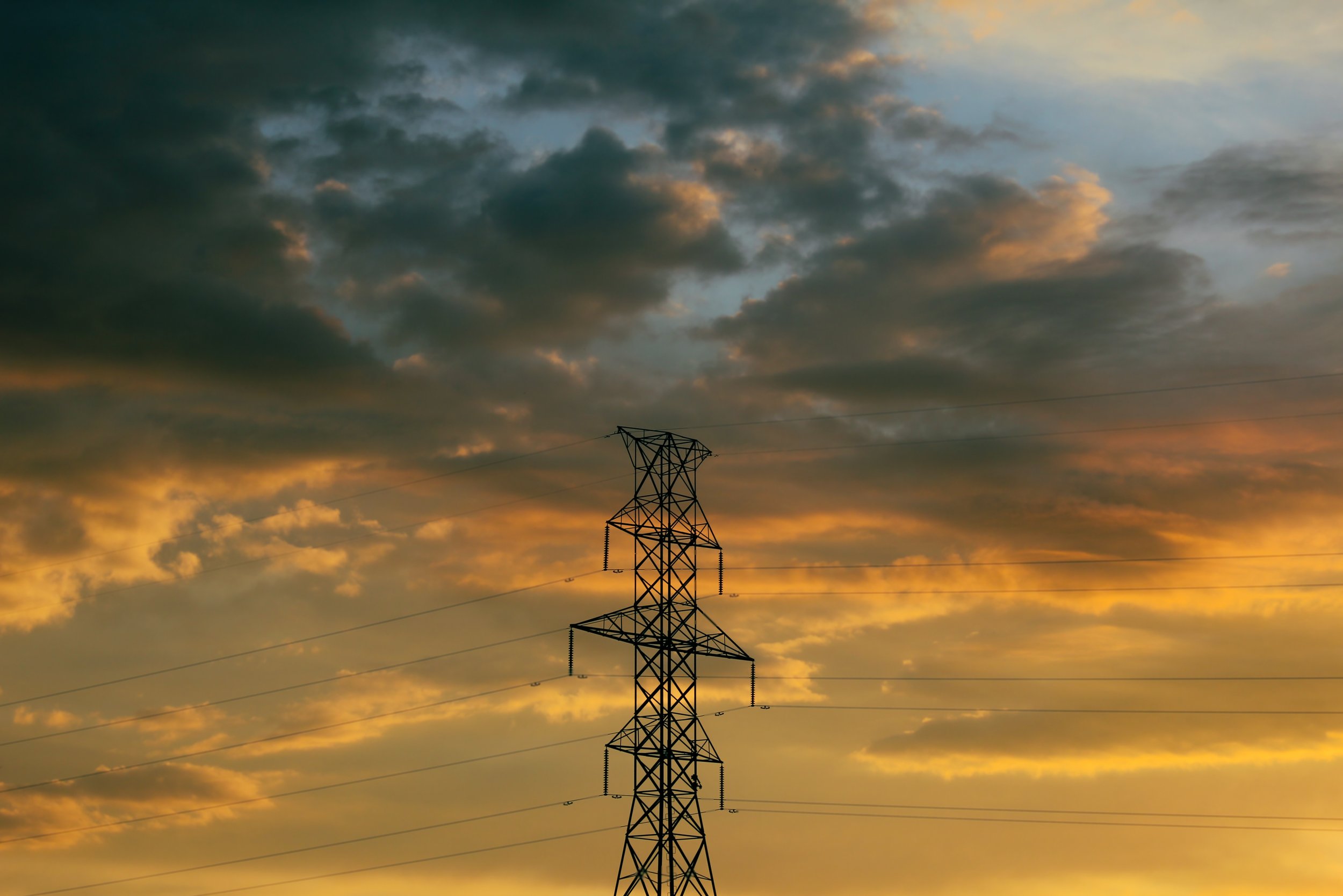 Power line tower against a cloudy sunset sky.