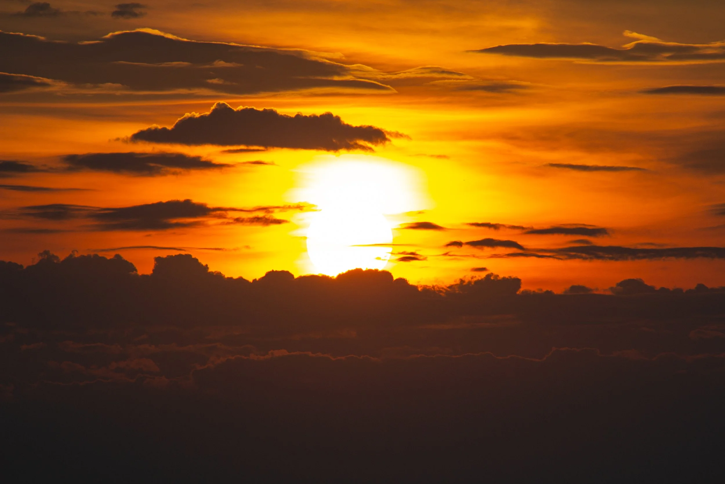 A sunset with the sun partly obscured by clouds, casting an orange and yellow glow across the sky.
