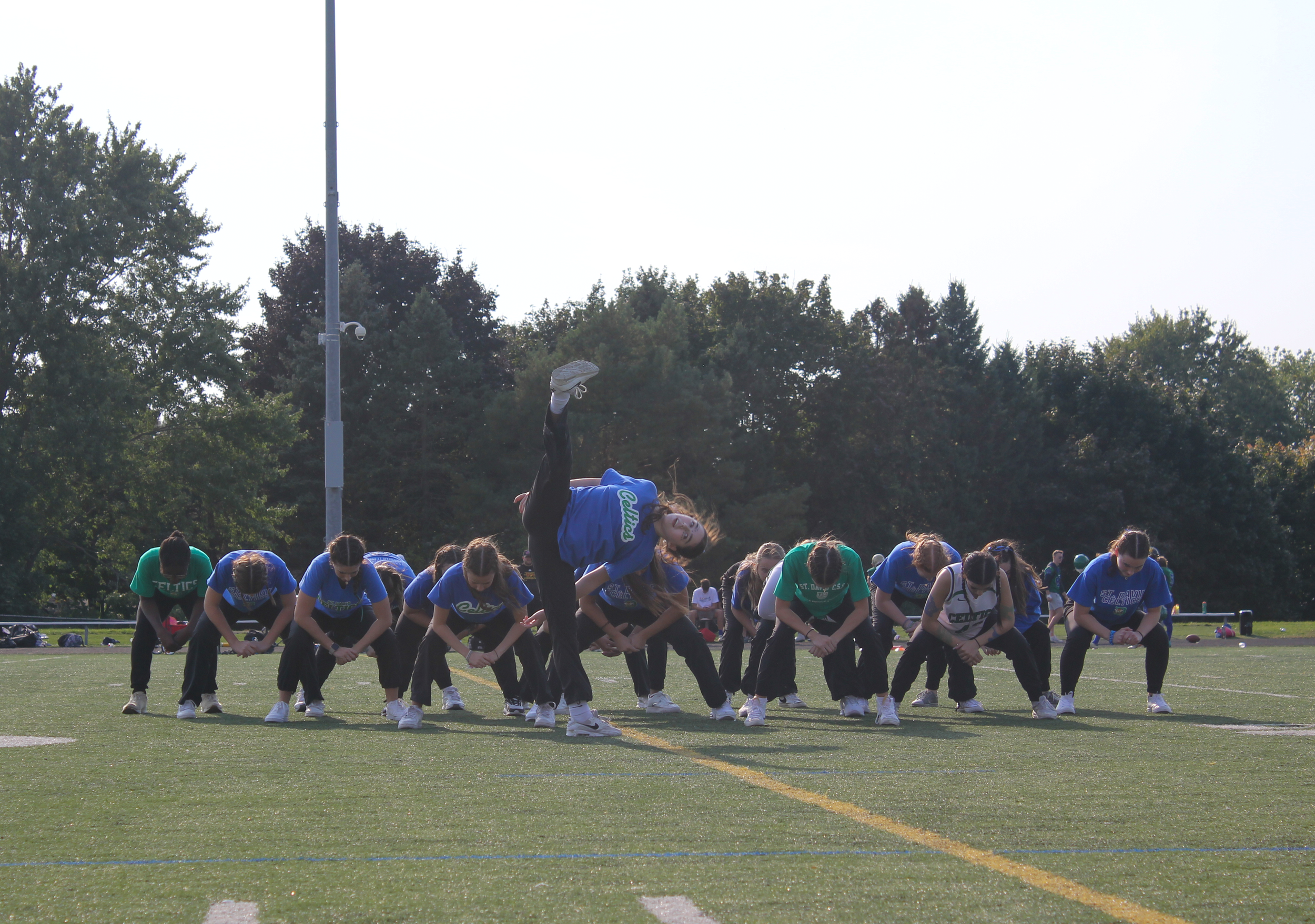 A group of female cheerleaders in blue and green uniforms performing a formation on a sports field during daytime.