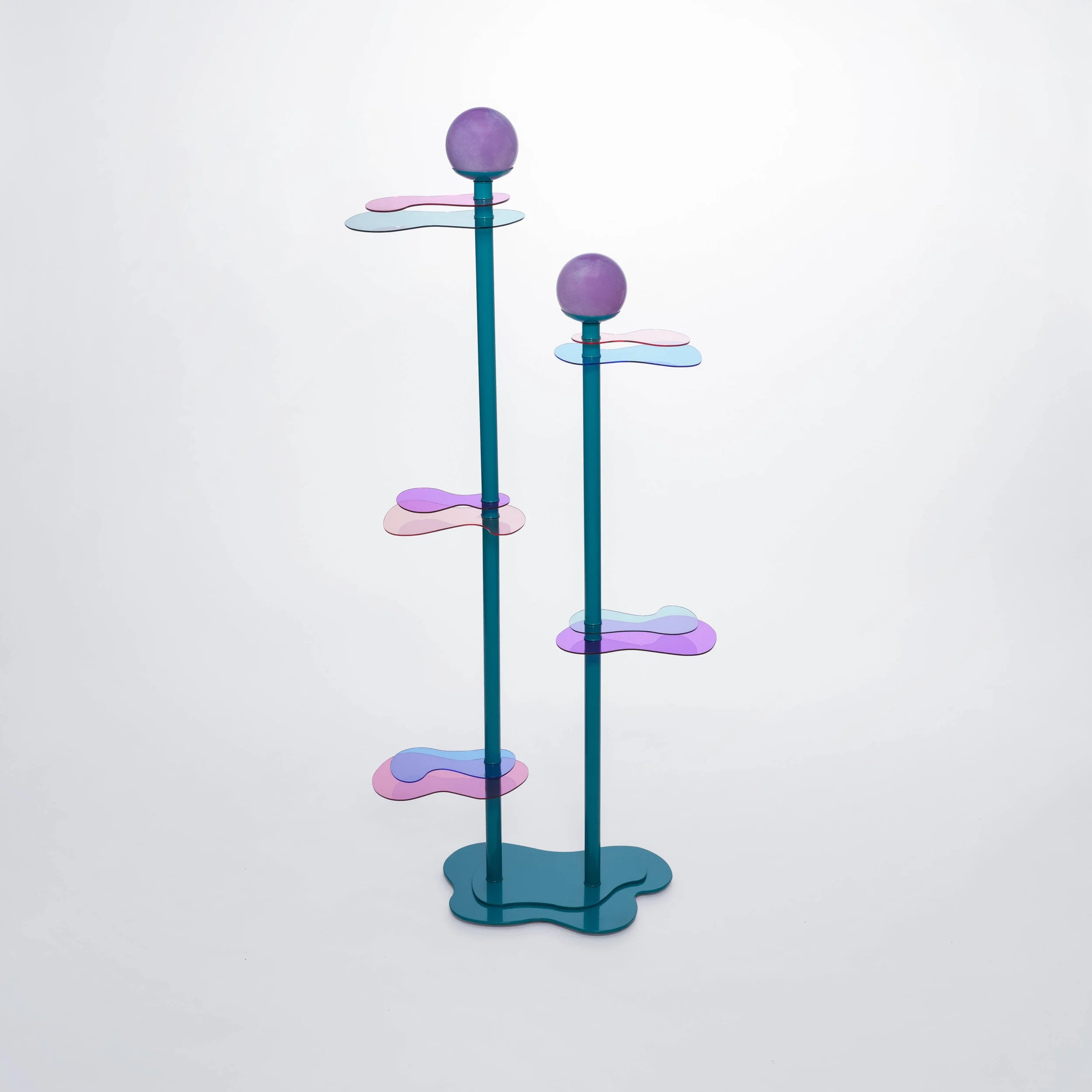 Colorful modern sculpture with two vertical blue poles ending with purple spheres, with layered, petal-shaped acrylic pieces in pink and purple attached along the poles, set against a plain white background.