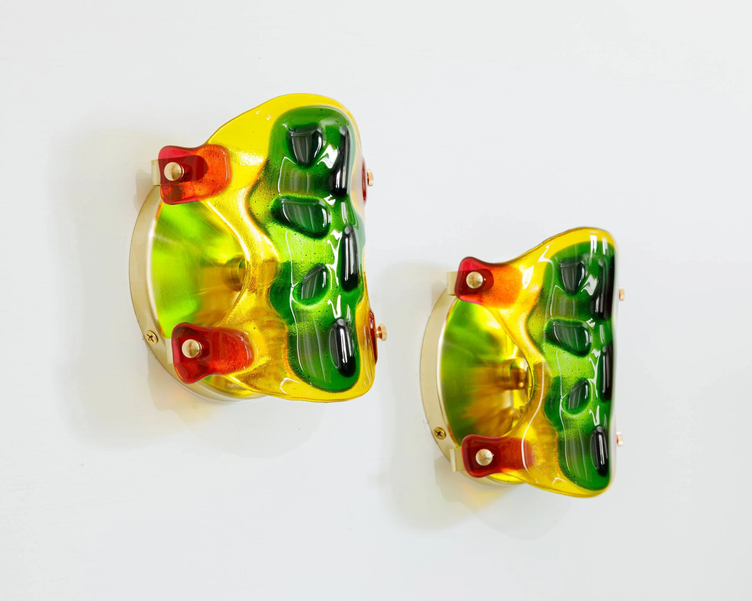 Two colorful vintage wall-mounted lamps with glass shades in green, yellow, and red, mounted on a white wall.