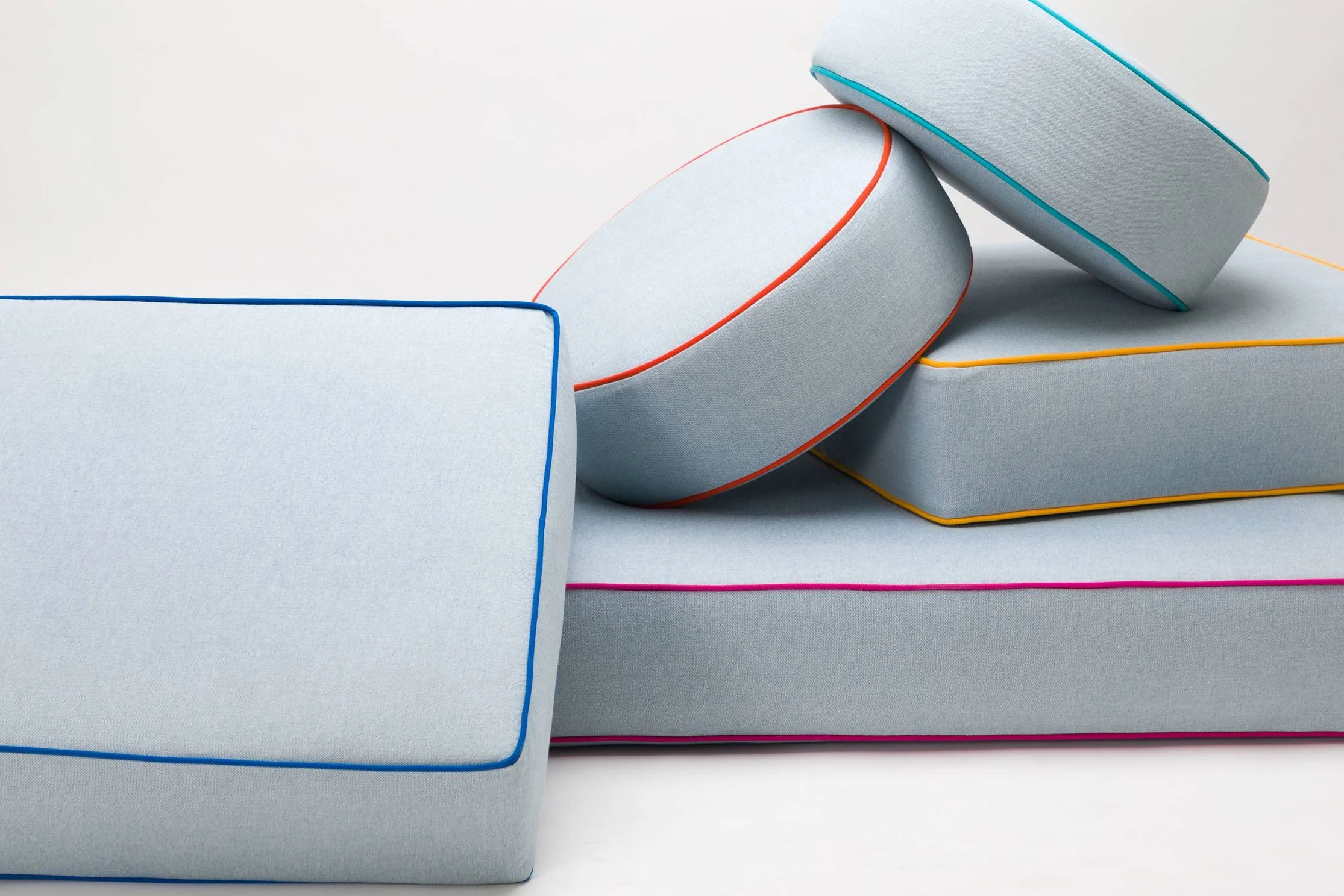 Stacked light-colored mattresses with colorful piping detail, some leaning on each other, on a white background.