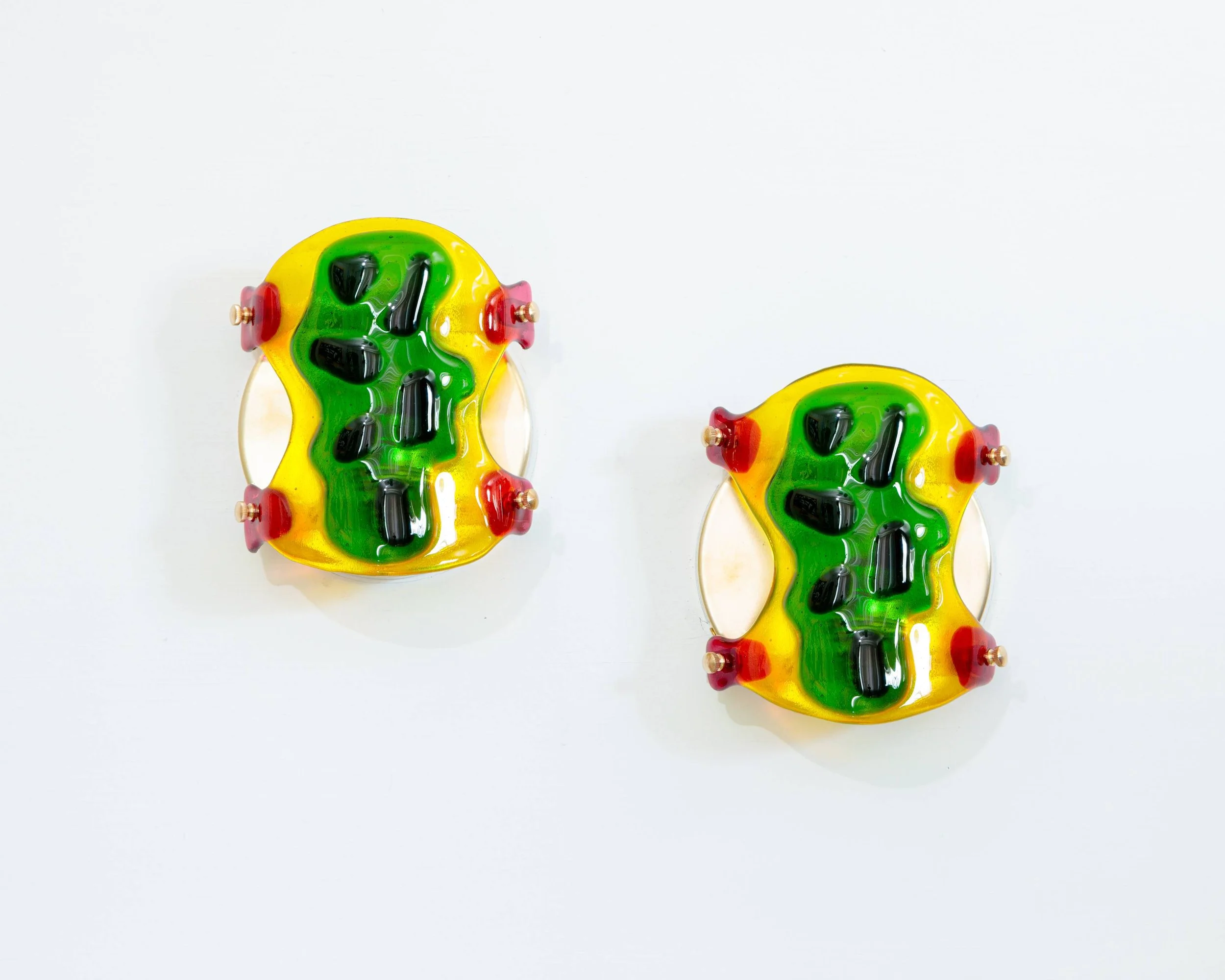 Colorful glass art pieces resembling yellow with green and red accents, placed on a white background.