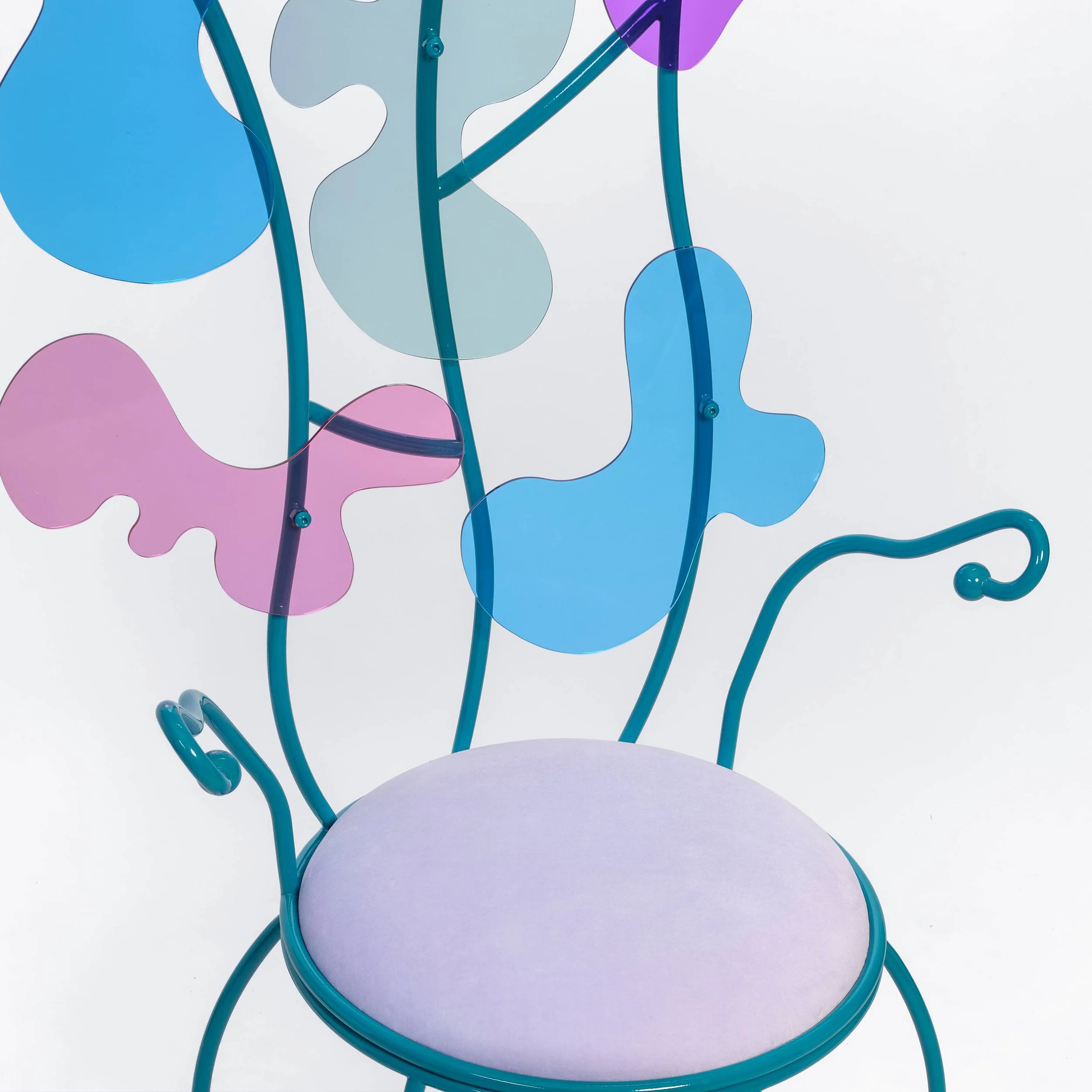 Colorful decorative chair with a pink cushioned seat, blue metal frame, and multicolored abstract acrylic shapes attached to the backrest, set against a plain white background.