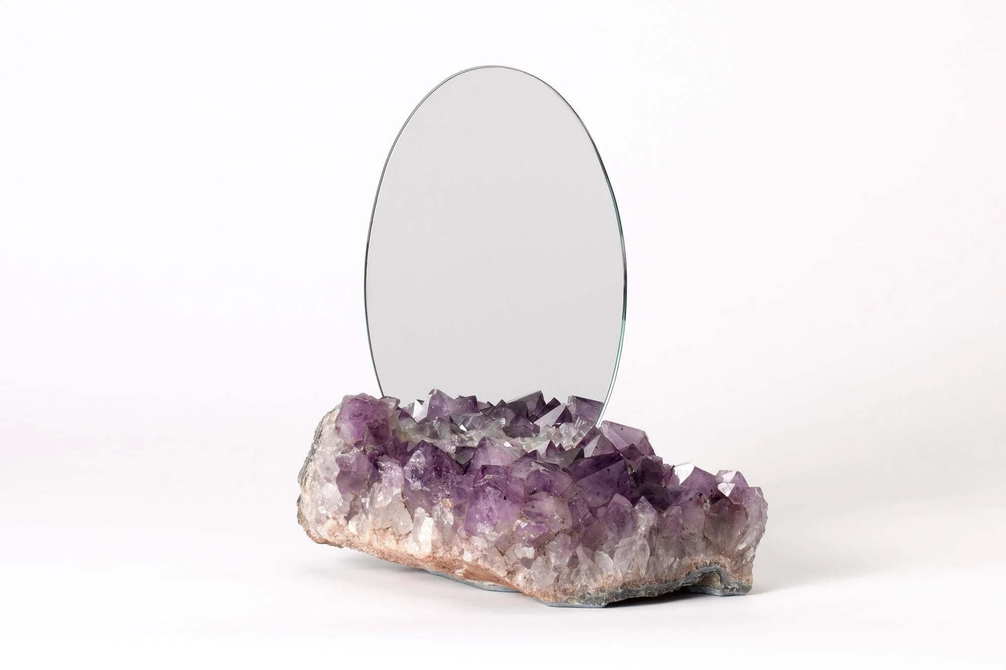 Mirror mounted on top of a purple and white crystal base, on a plain white background.