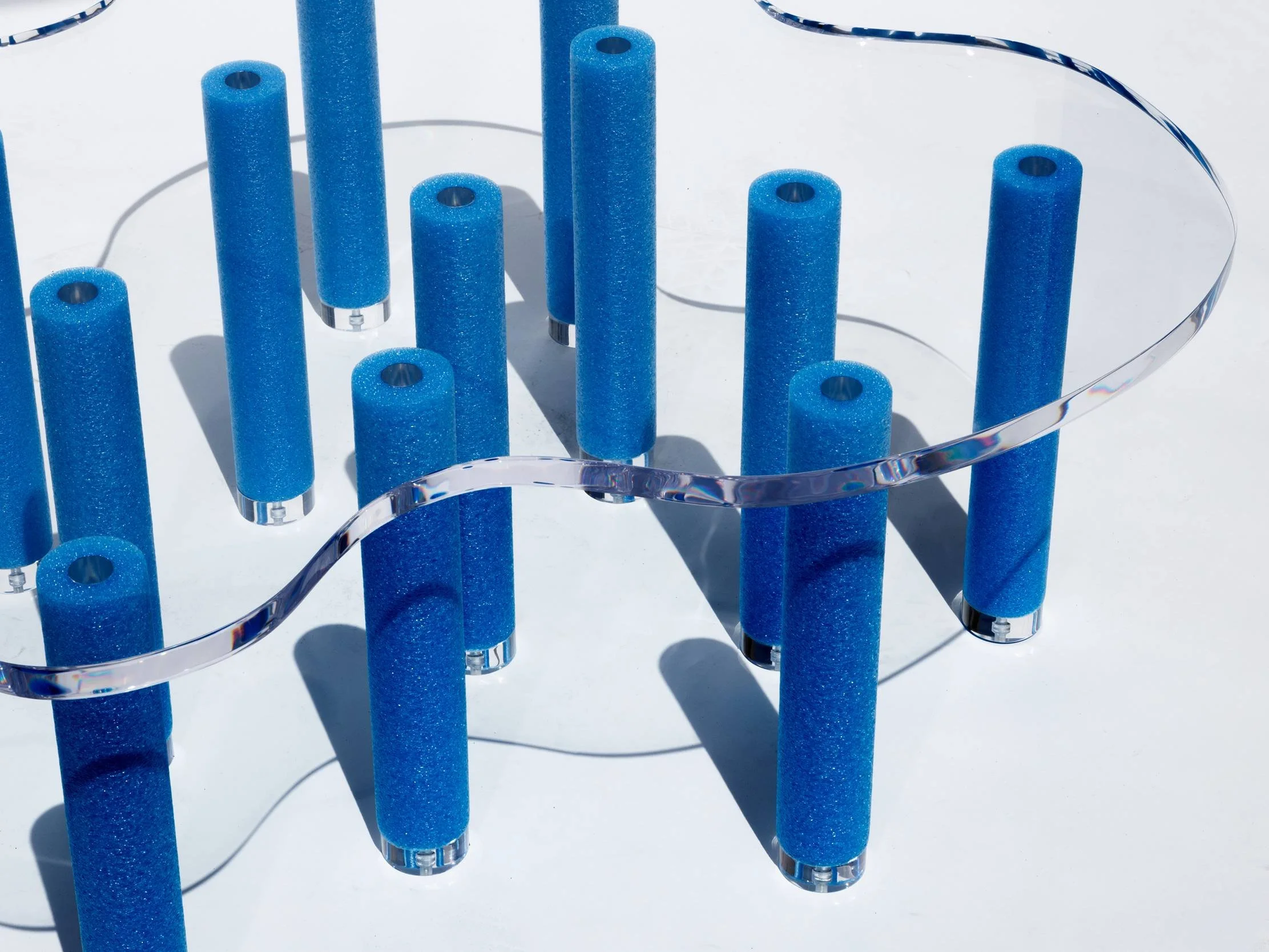 Blue foam rollers arranged on a transparent wavy stand with shadows cast on a white surface.