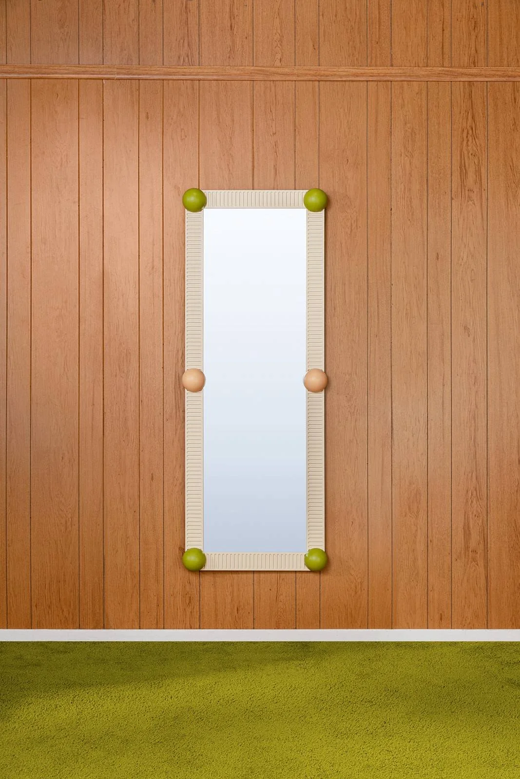 Full-length vertical mirror with a beige frame, mounted on a wooden wall with green and peach-colored decorative spheres at each corner, next to a green carpeted floor.