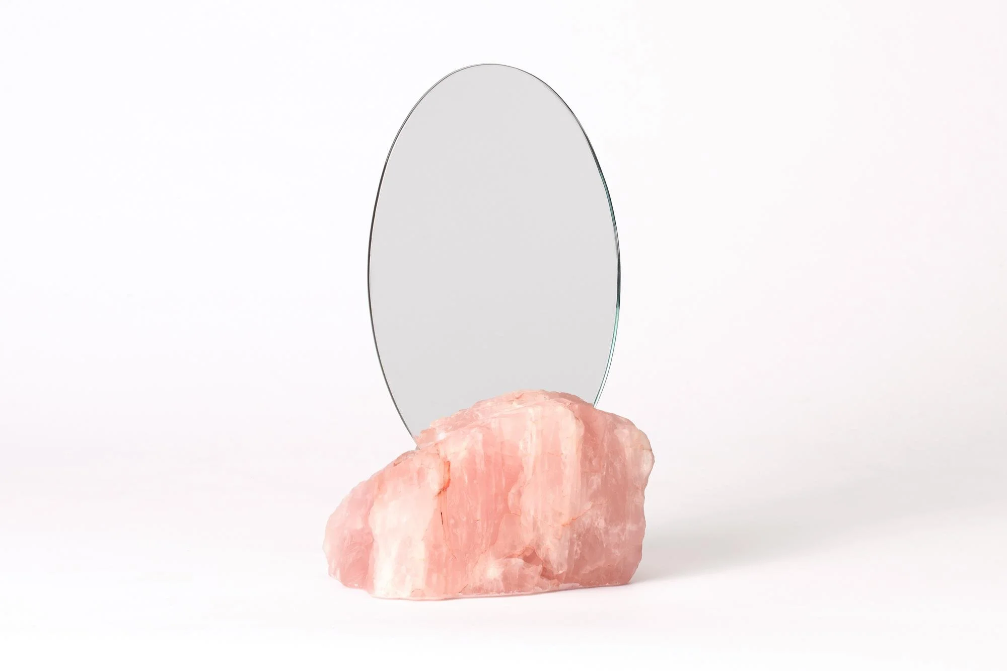 A small oval mirror standing on a pink Himalayan salt crystal