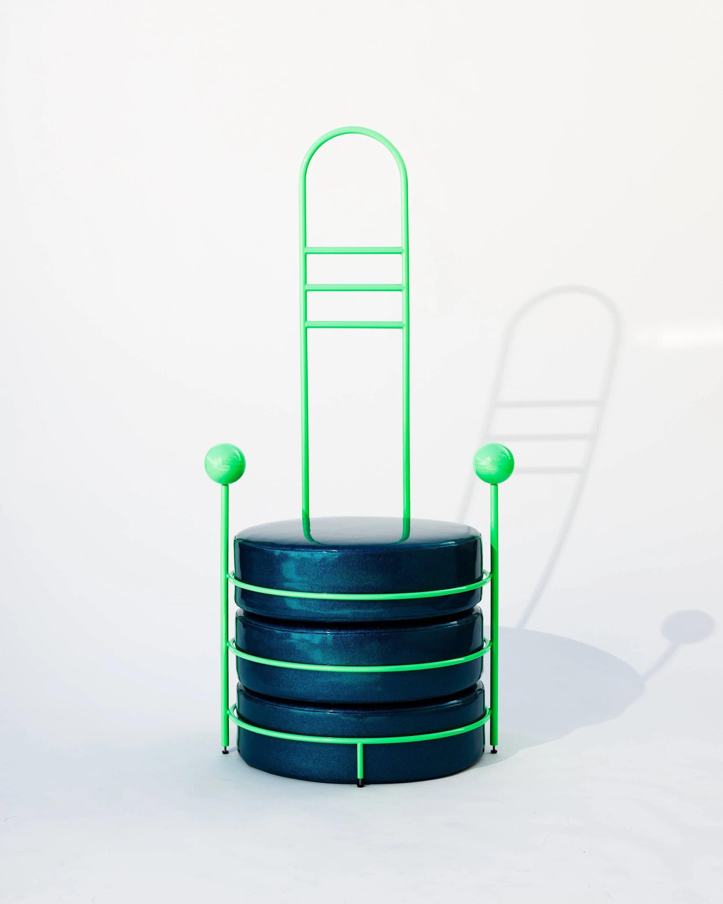 A modern chair made with stacked black cushions and a green metal frame with decorative spheres on the sides and a tall backrest.