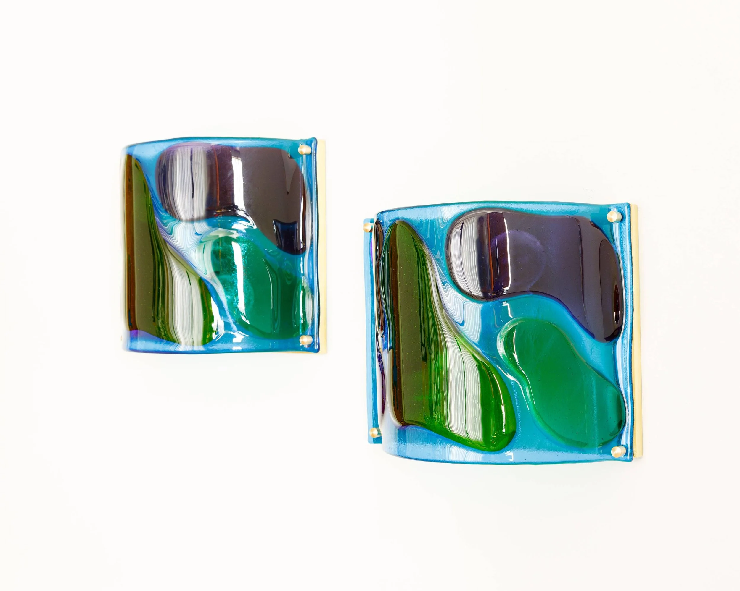 Two colorful glass art pieces with abstract swirling patterns in blue, green, black, and white, mounted on a white background.