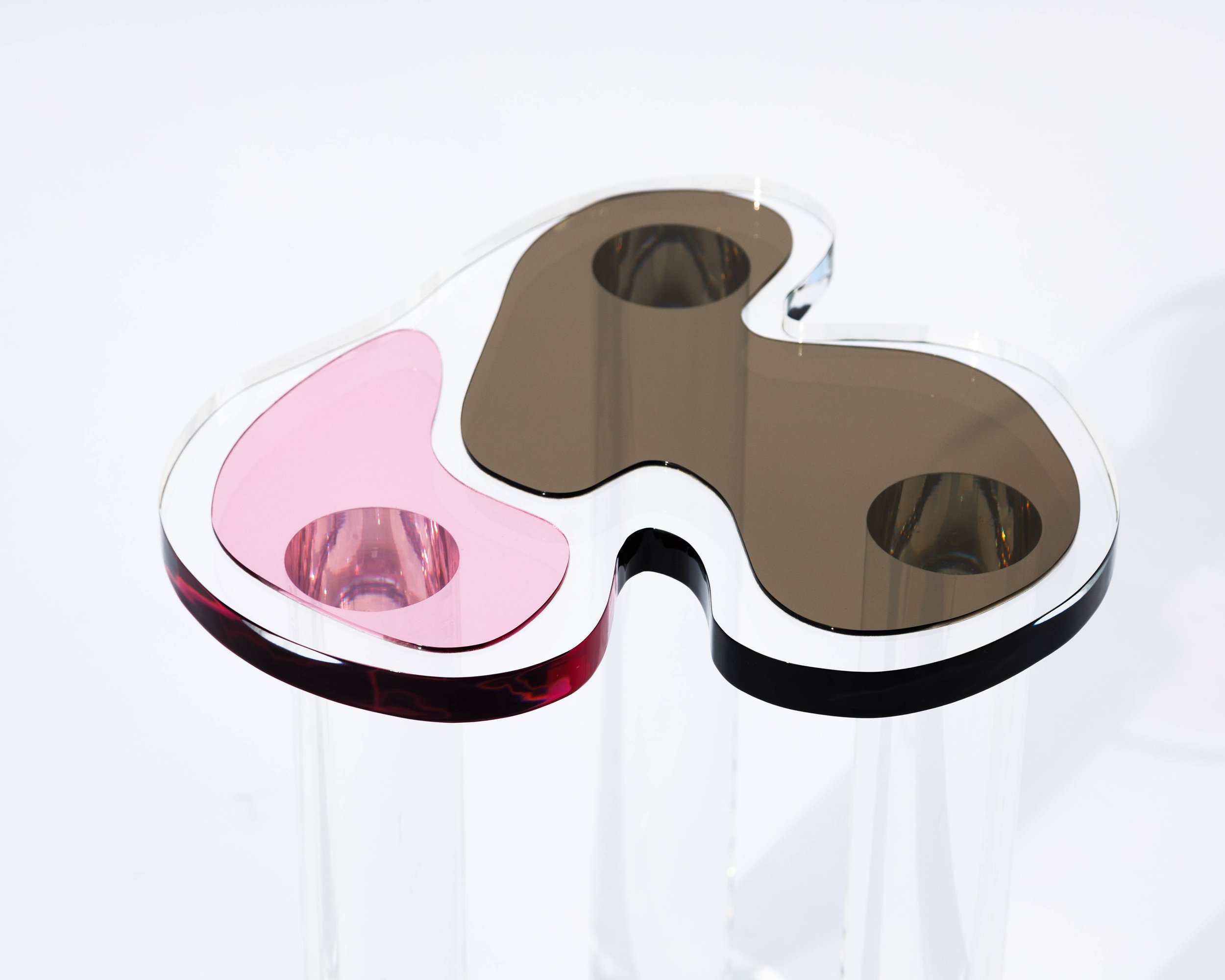 A modern, multi-colored butterfly-shaped object with two black, reflective sections and two pink, transparent sections, placed on a clear, stand.