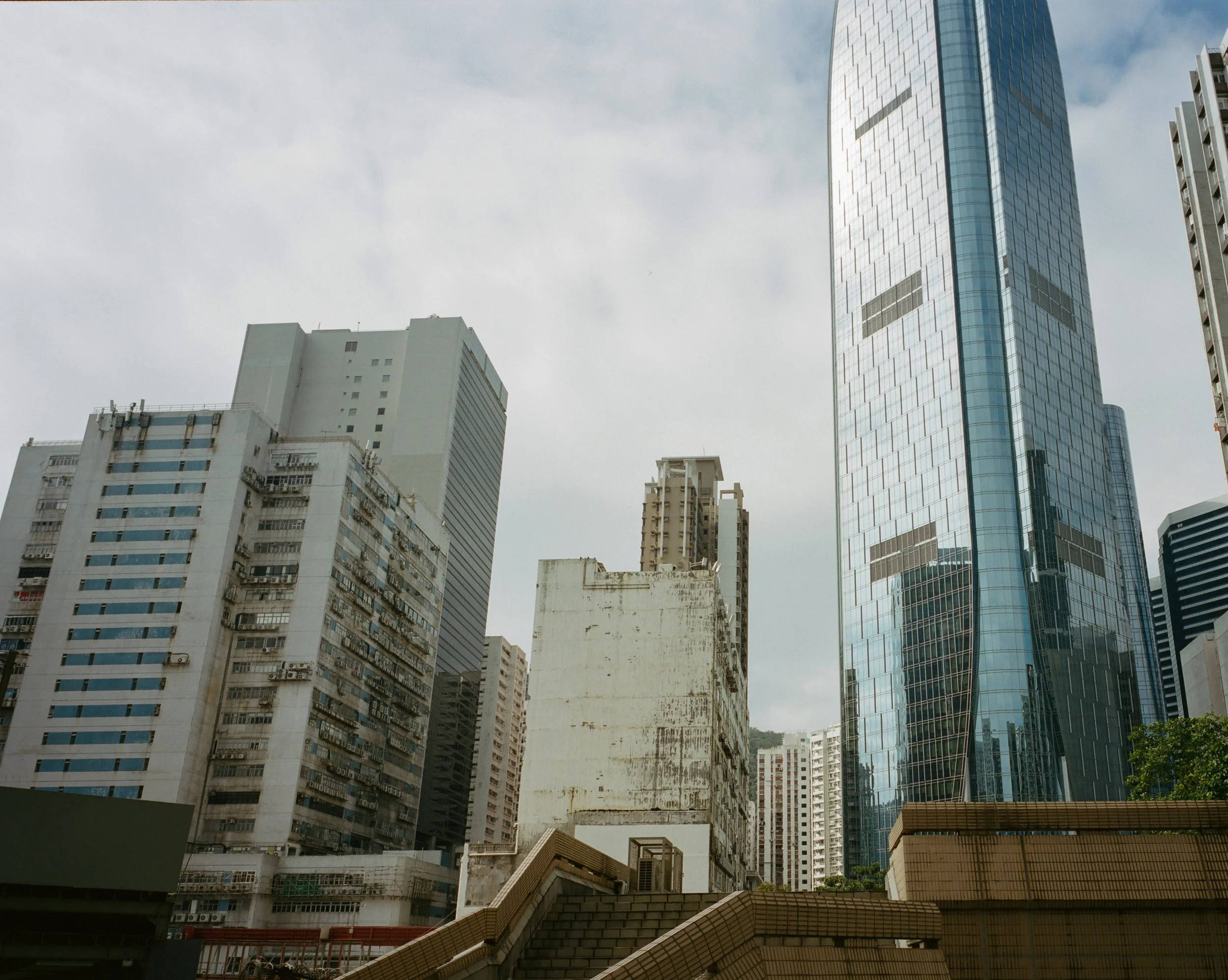 Cityscape featuring a mix of old and new skyscrapers, including a modern glass tower reflecting the sky, with a cloudy sky overhead.