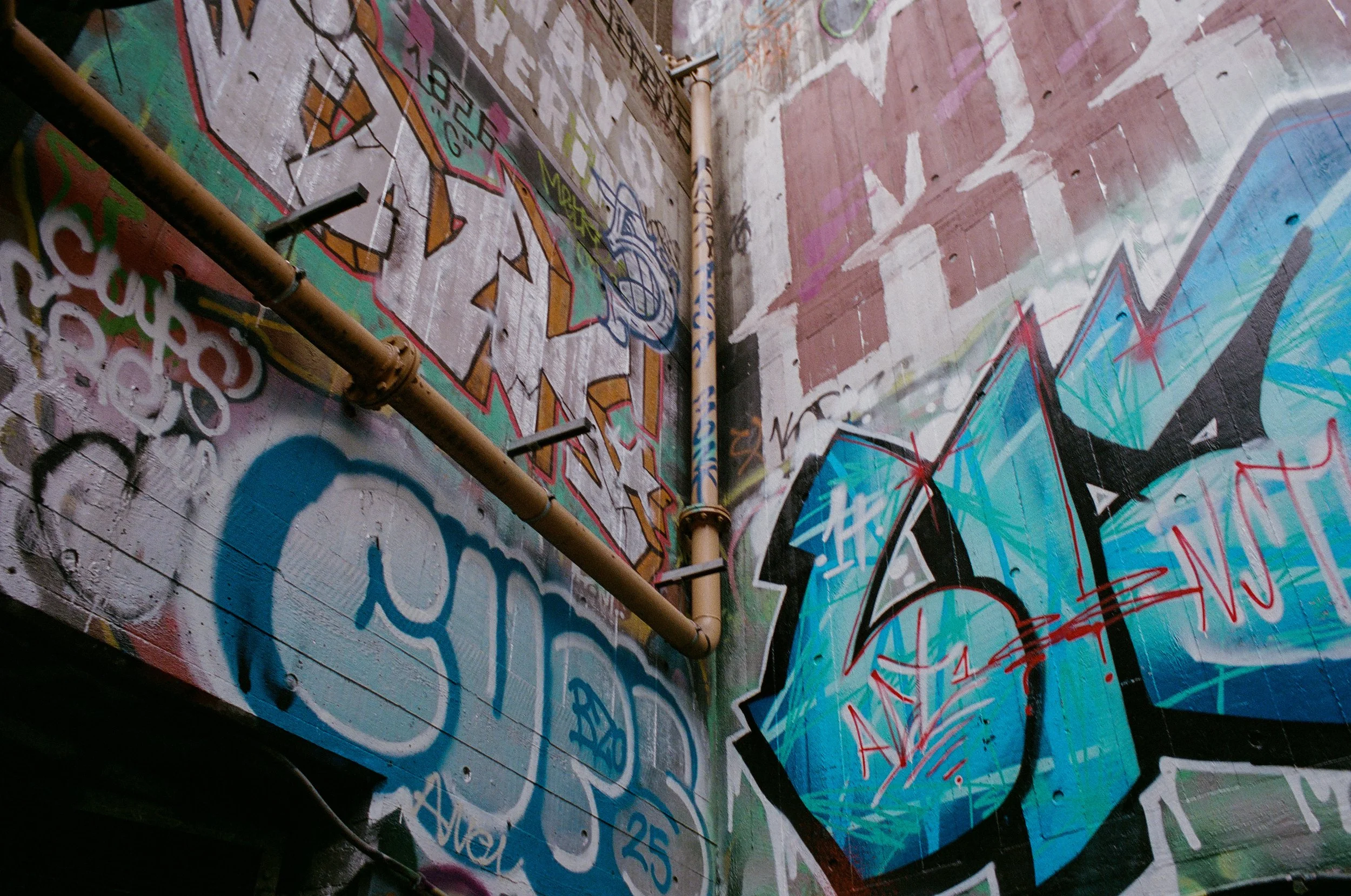 Graffiti art on a brick wall featuring colorful stylized letters and a brown pipe running diagonally across the scene.