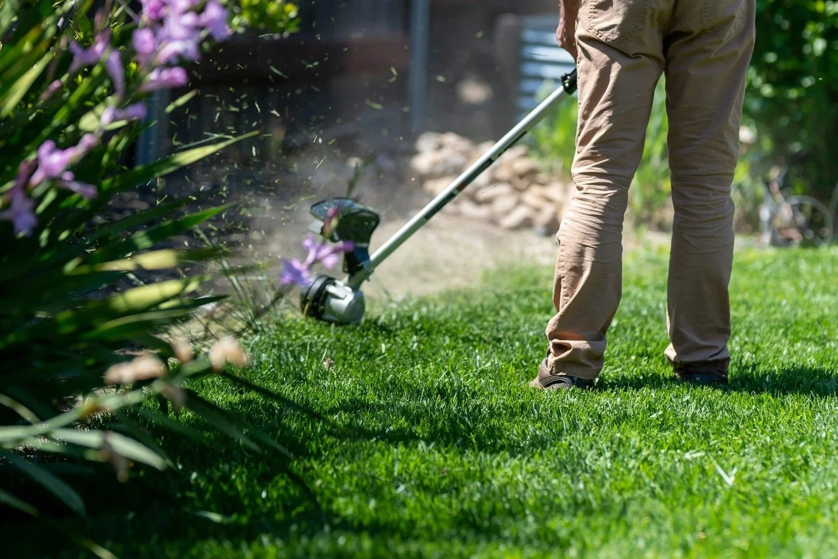 Person trimming grass with a weed trimmer on a lawn representing the type of maintenance offered by Aquila Landscapes Design & Build.