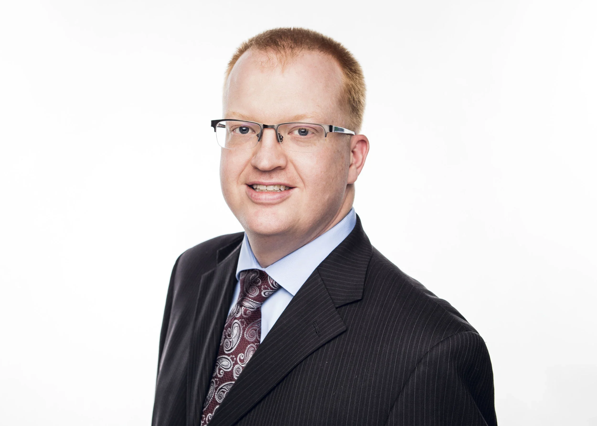 A man in a suit with glasses smiling against a white background.
