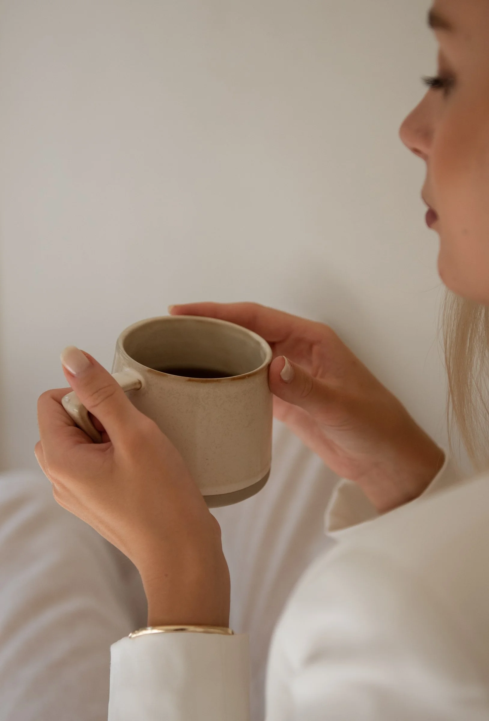 Person holding a beige ceramic mug filled with dark coffee or tea, with a plain white background.