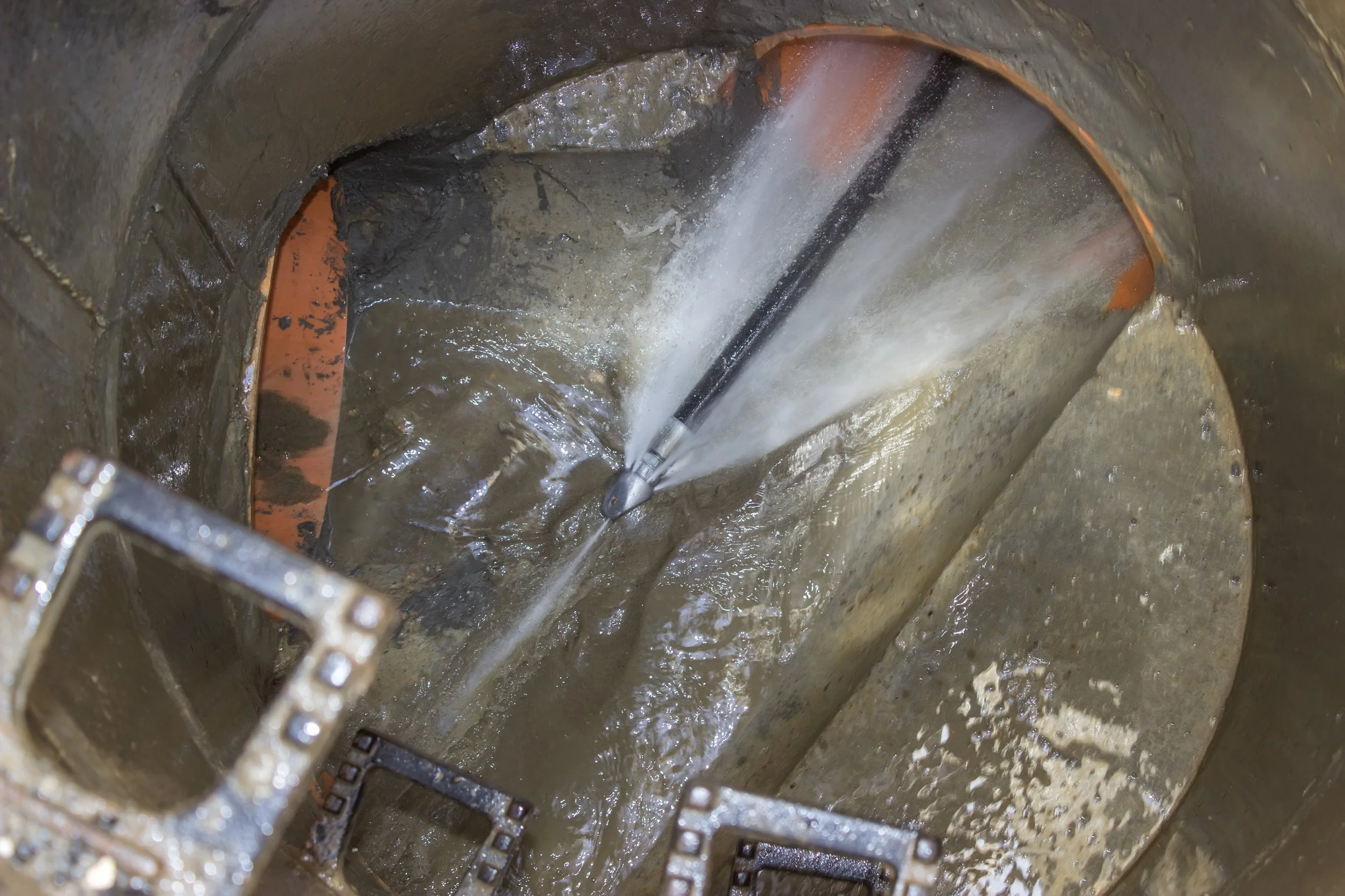 A close-up view of industrial water jet cleaning equipment spraying water inside a pipe.
