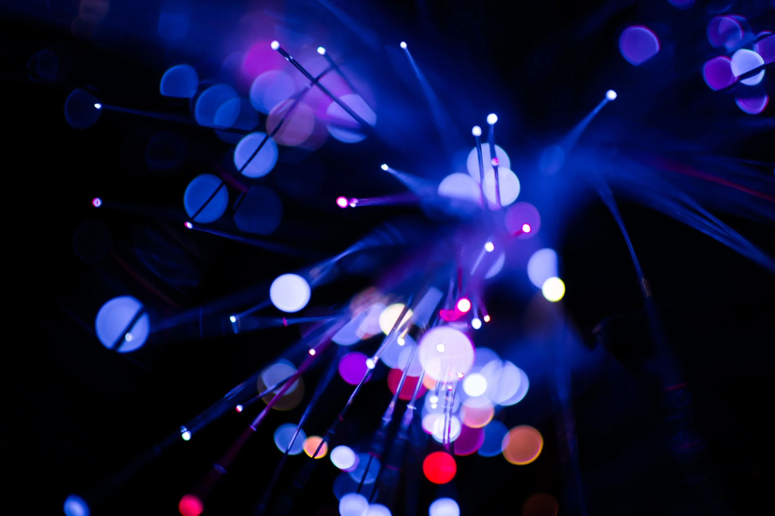 Abstract image of fiber optic lights in blue, purple, pink, yellow, and red, with bokeh effect and light streaks.